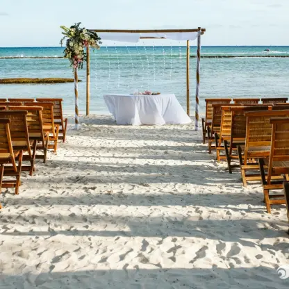 Beachfront wedding ceremony with wooden chairs and floral arch at Grand Velas Riviera Maya, Riviera Maya