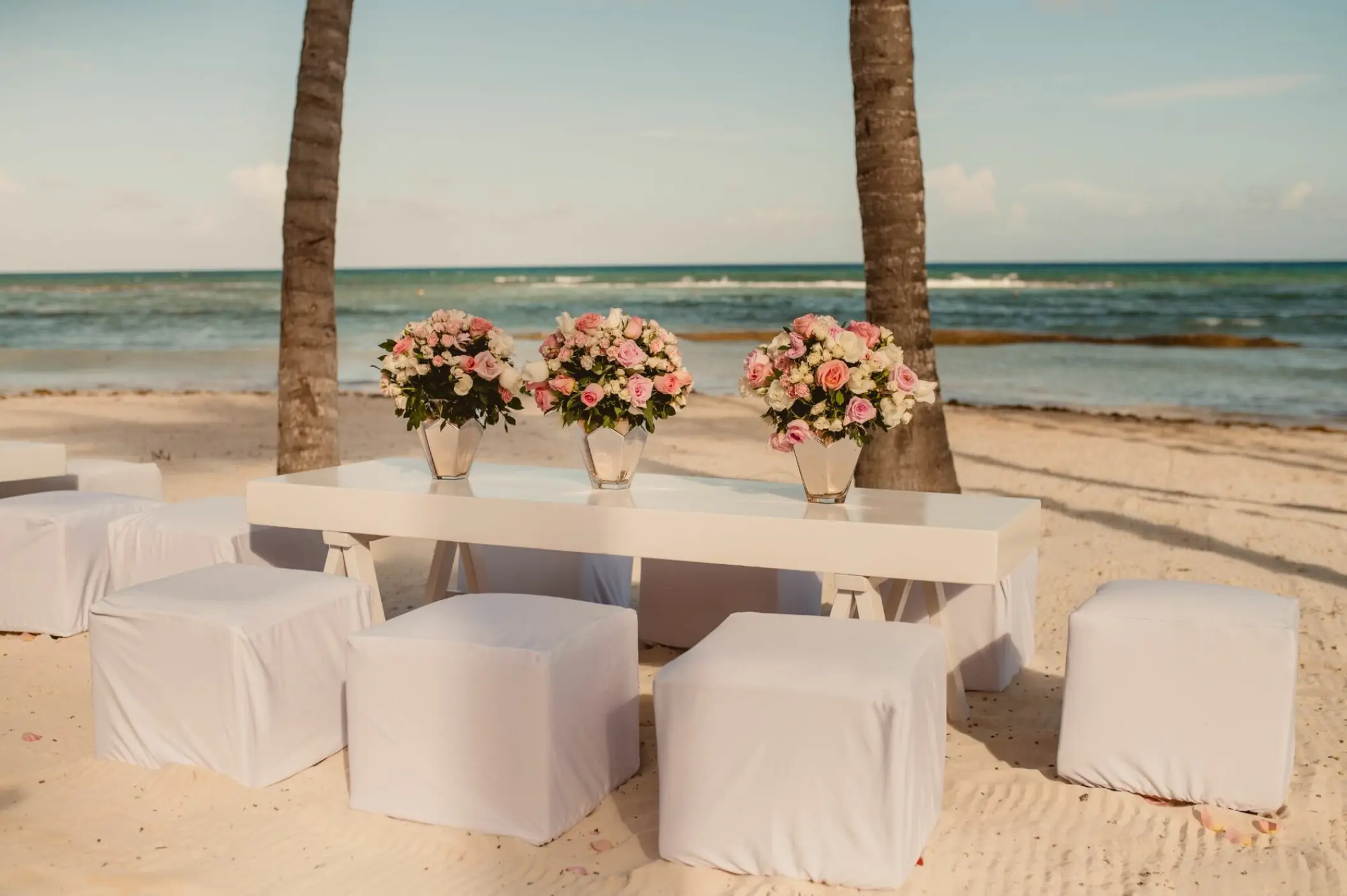 White lounge furniture and floral centerpieces for a beach wedding at Grand Velas Riviera Maya