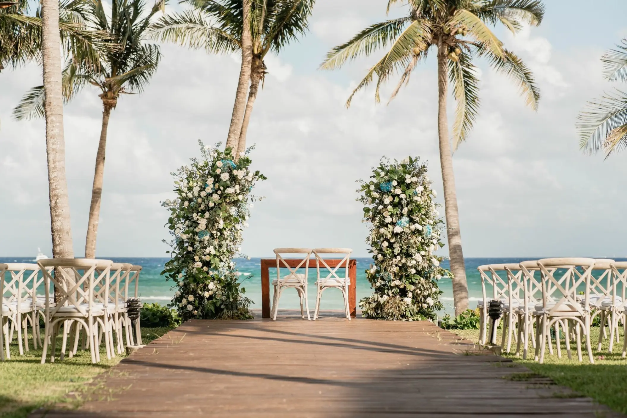 Beachfront wedding ceremony setup with floral pillars and crossback chairs at Grand Velas Riviera Maya