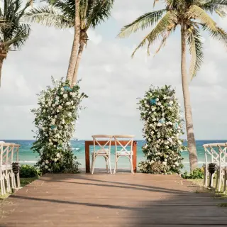 Beachfront wedding ceremony setup with floral pillars and crossback chairs at Grand Velas Riviera Maya