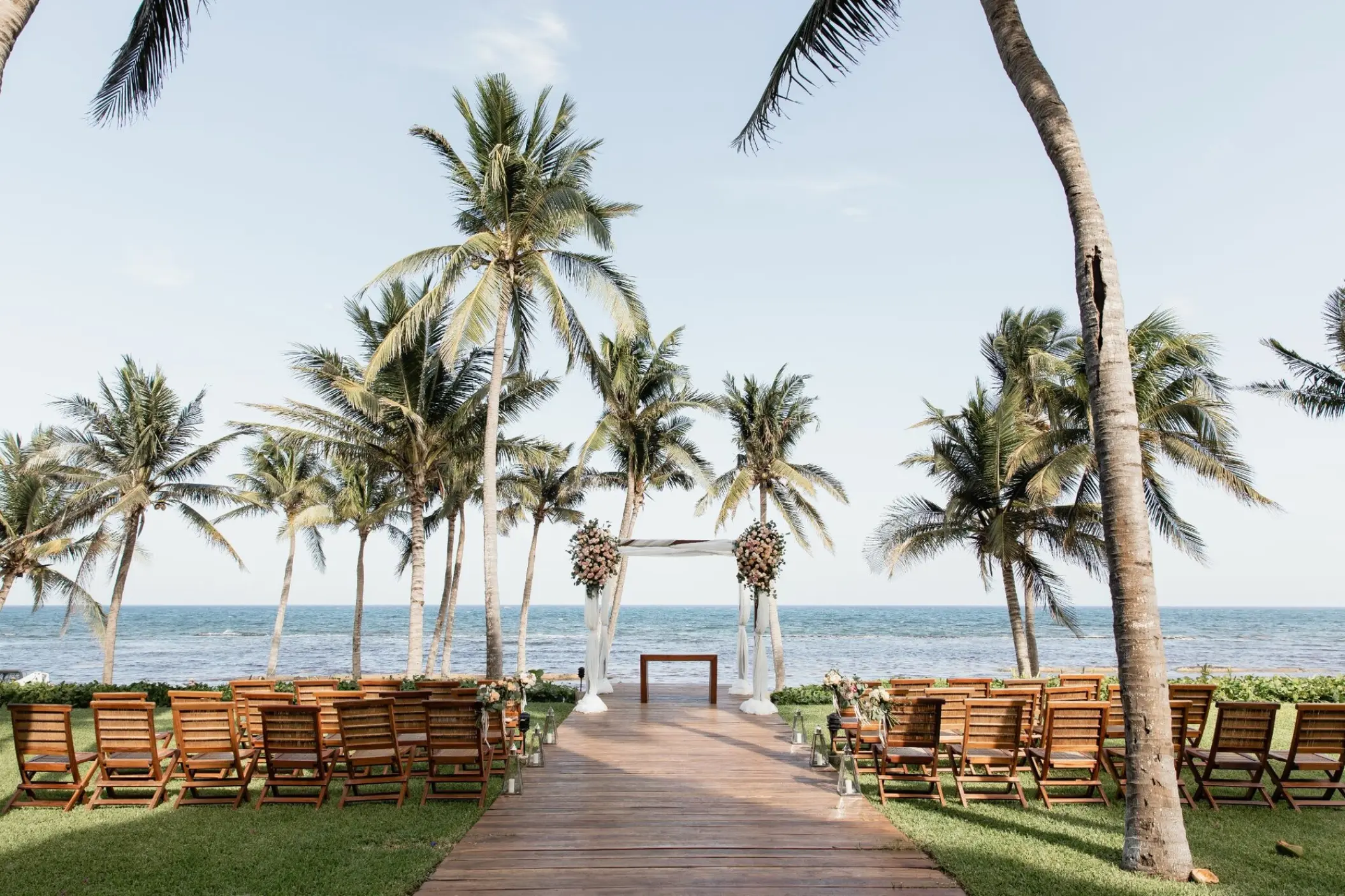 Beachfront wedding ceremony with a wooden aisle and floral arch at Grand Velas Riviera Maya
