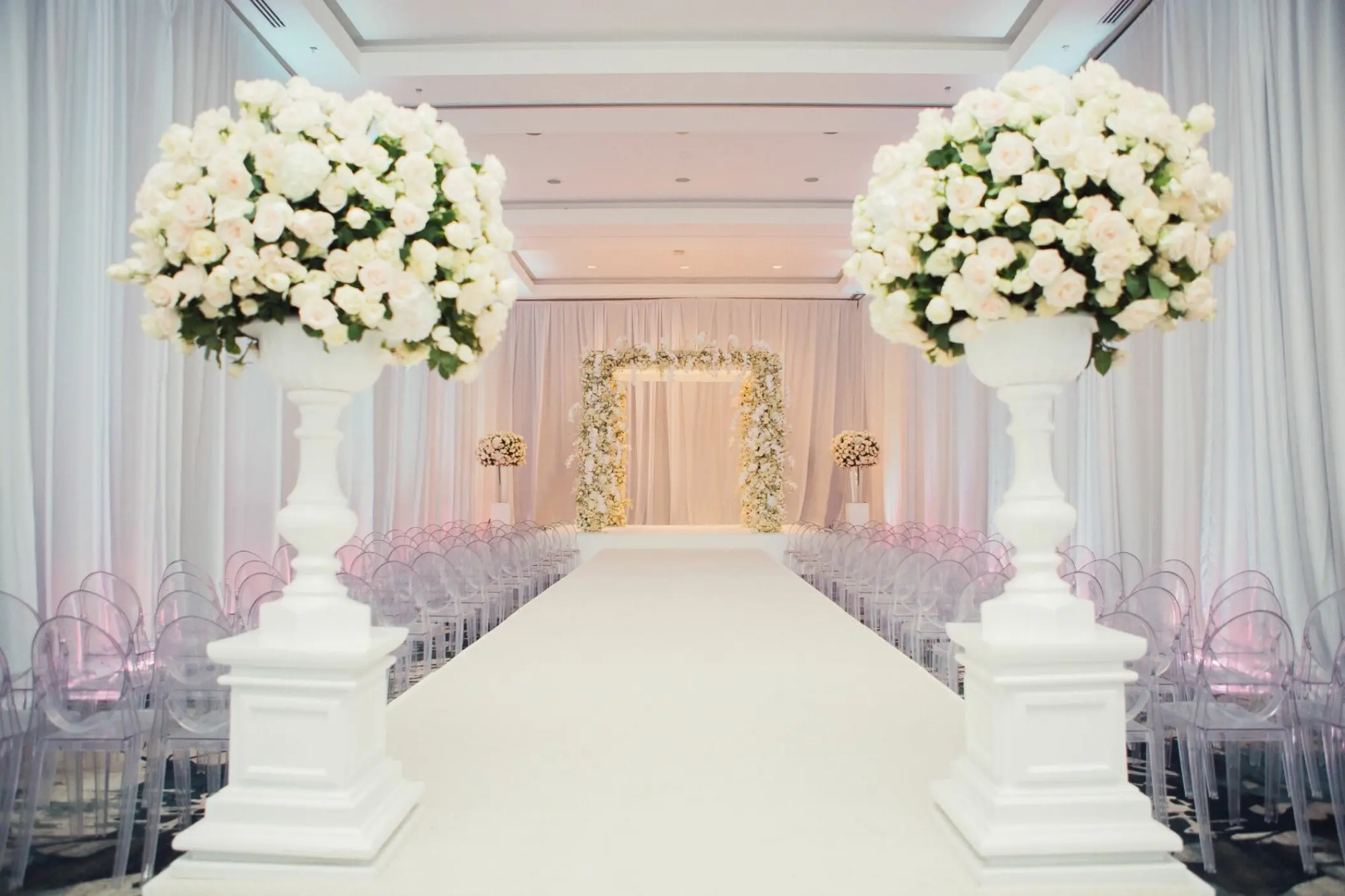 Indoor wedding ceremony with a white aisle and floral arch at Grand Velas Riviera Maya