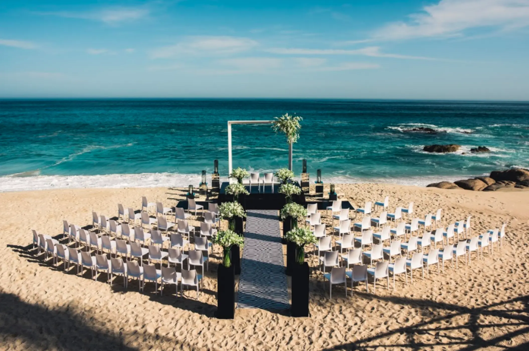 Beachfront wedding ceremony with white chairs and floral pillars at Grand Velas Los Cabos, Cabo San Lucas