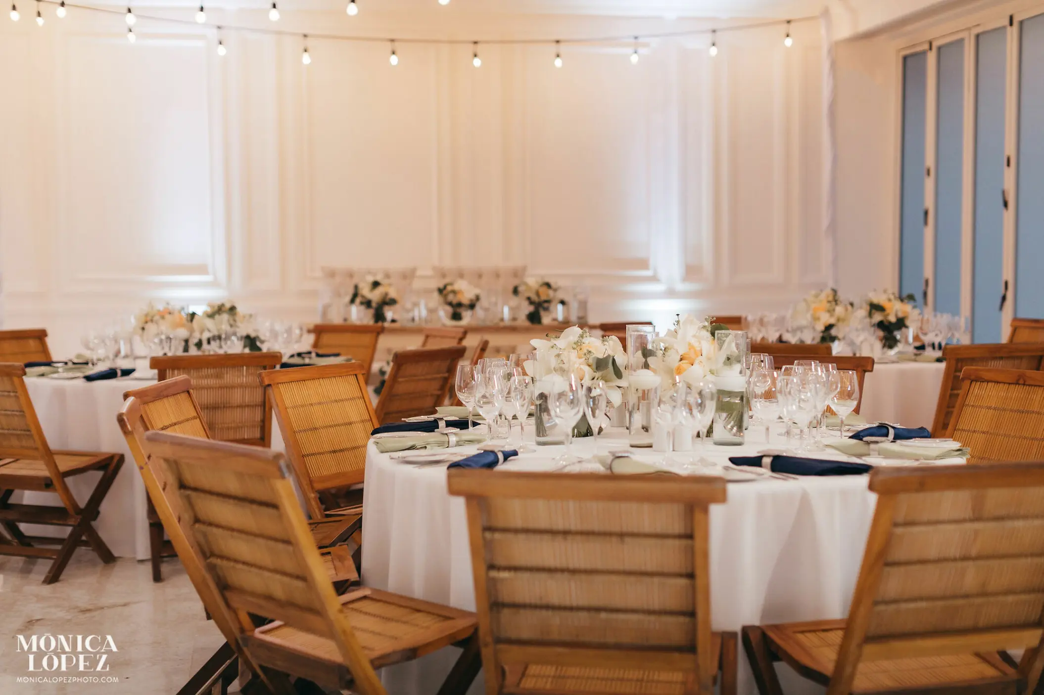Indoor wedding reception with round tables and wooden chairs at Grand Velas Riviera Maya