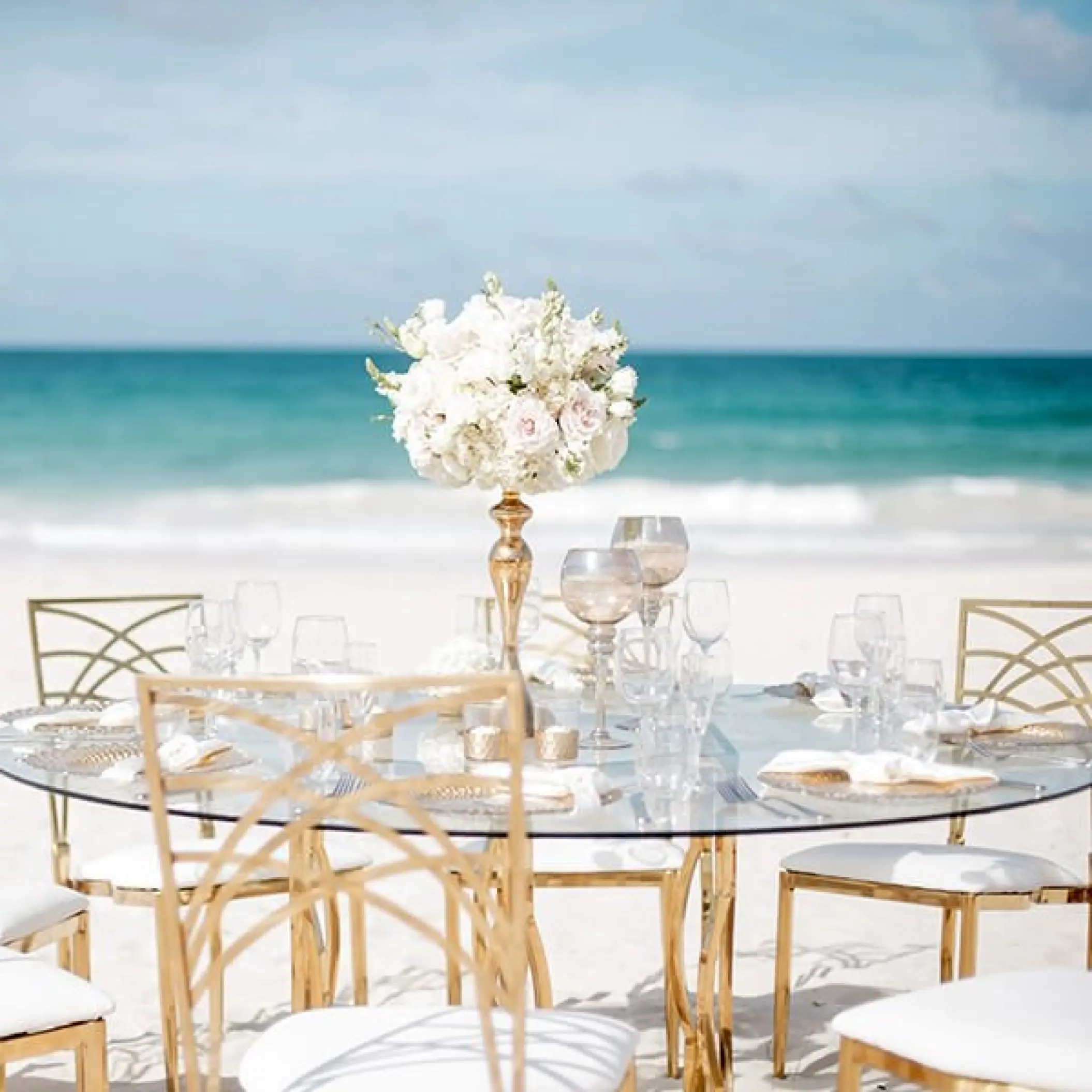 Beachfront wedding reception table with gold chairs and white flowers at Hard Rock Riviera Maya