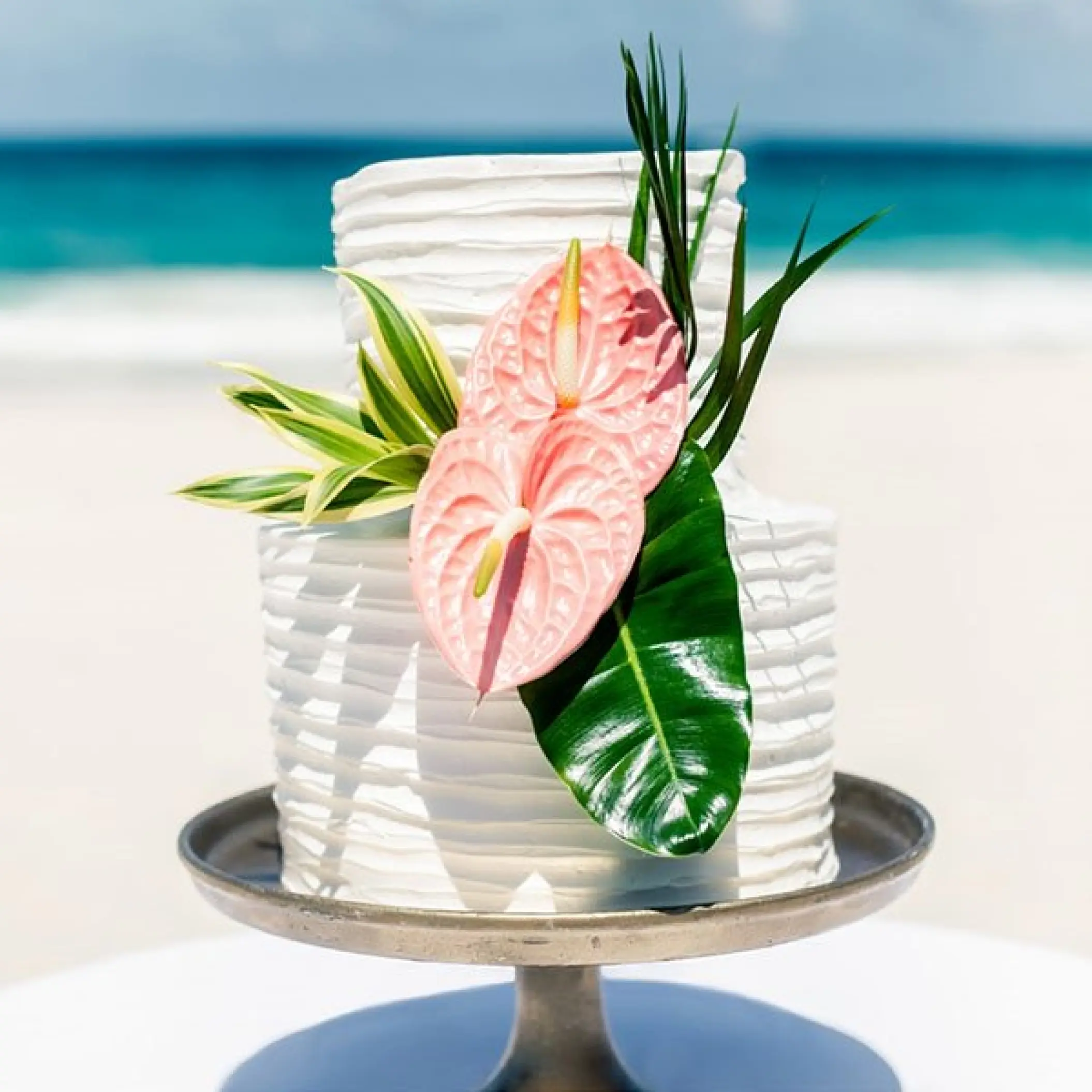 White tiered wedding cake with pink flowers on a beach at Hard Rock Riviera Maya