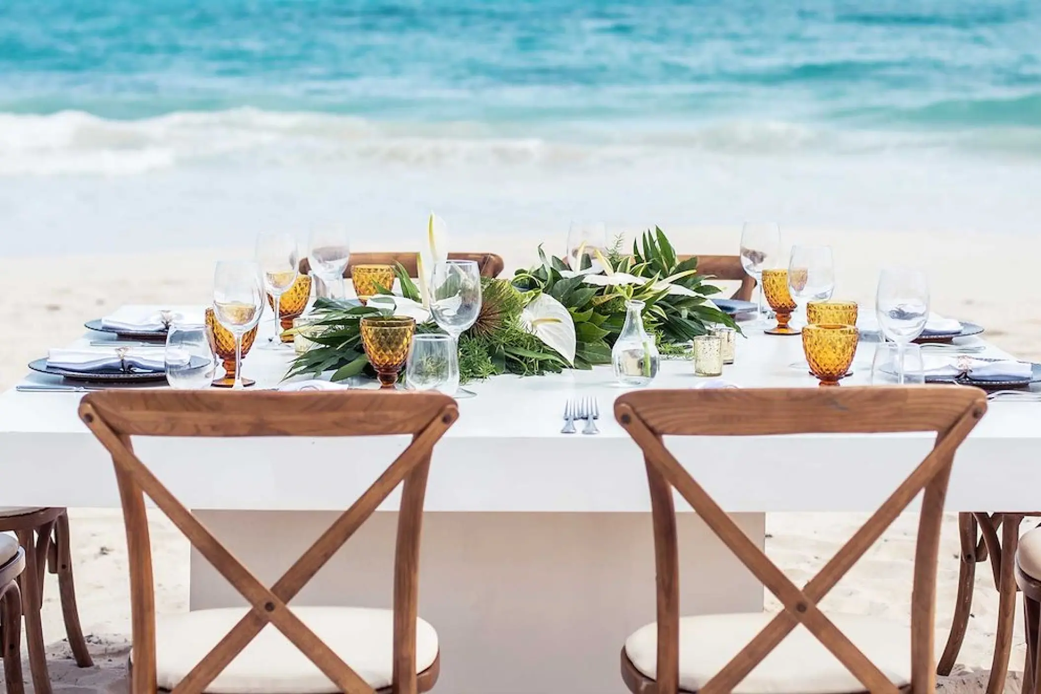 Boho beach wedding reception table with amber glassware and wooden chairs at Hard Rock Cancun