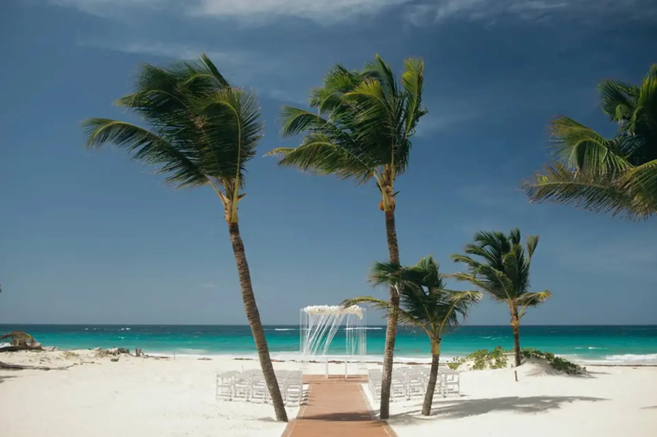 Beachfront wedding ceremony with white chairs and palm trees at Hard Rock Hotel Punta Cana, Punta Cana