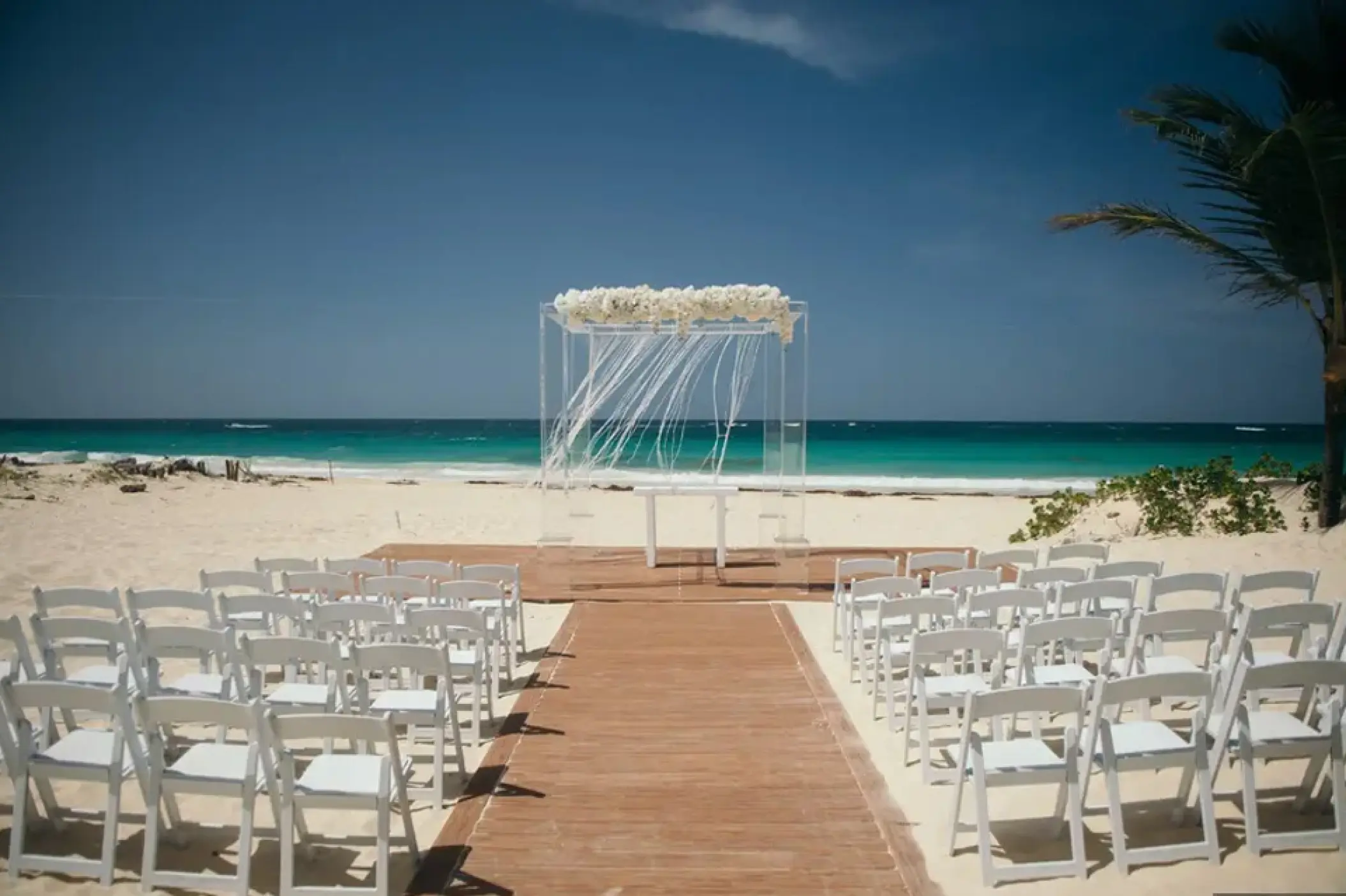 Beachfront wedding ceremony with white chairs and floral arch at Hard Rock Punta Cana, Punta Cana