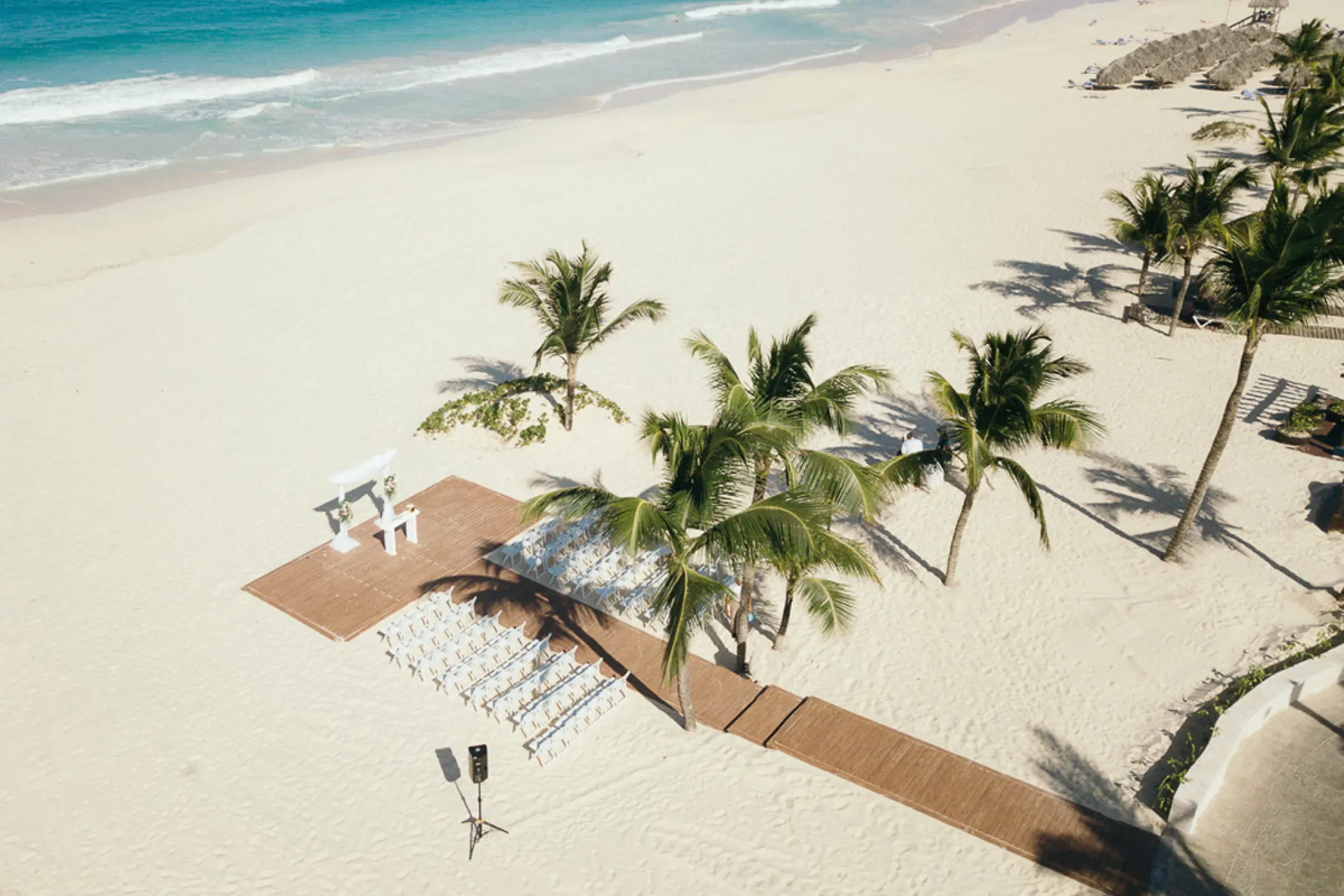 Aerial view of a beach ceremony setup with a wooden walkway and palm trees at Hard Rock Punta Cana