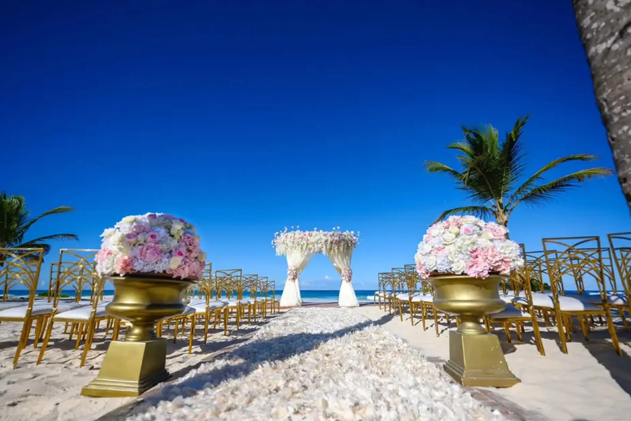 Beachfront wedding ceremony with a floral gazebo and gold chairs at Hard Rock Punta Cana