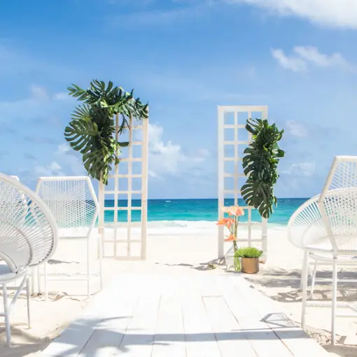 Beachfront wedding ceremony setup with white chairs and floral arches at Hard Rock Riviera Maya
