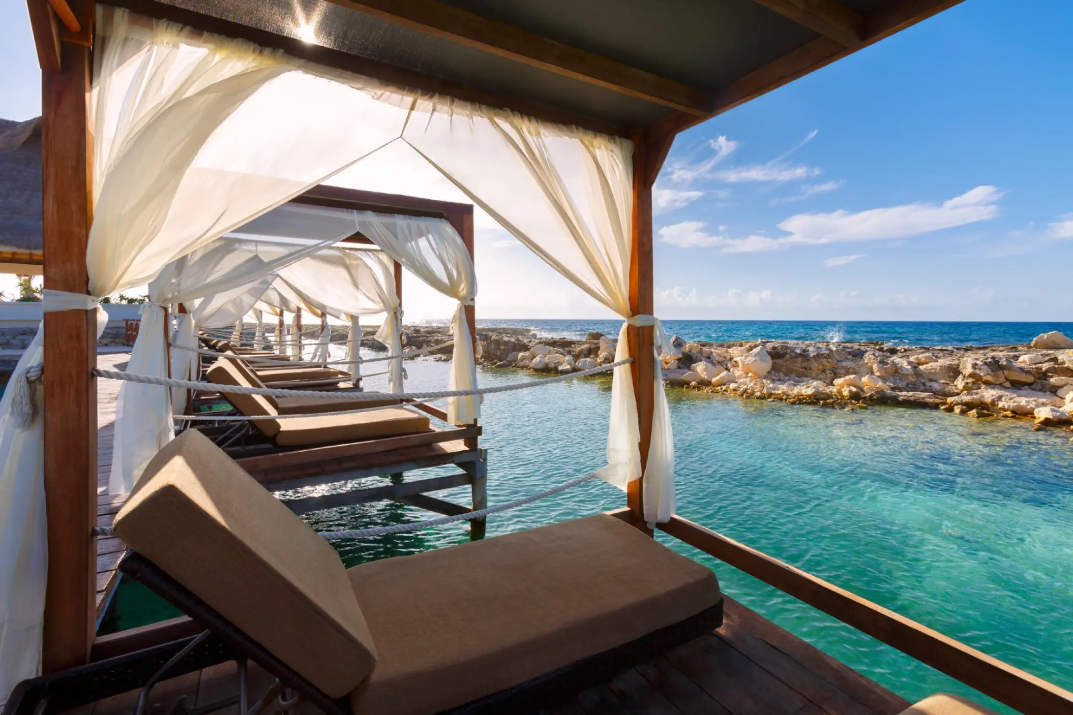Private beach cabanas with sun loungers over the water at Hard Rock Riviera Maya