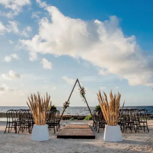 Beachfront wedding ceremony with a triangle arch and pampas grass at Hard Rock Riviera Maya