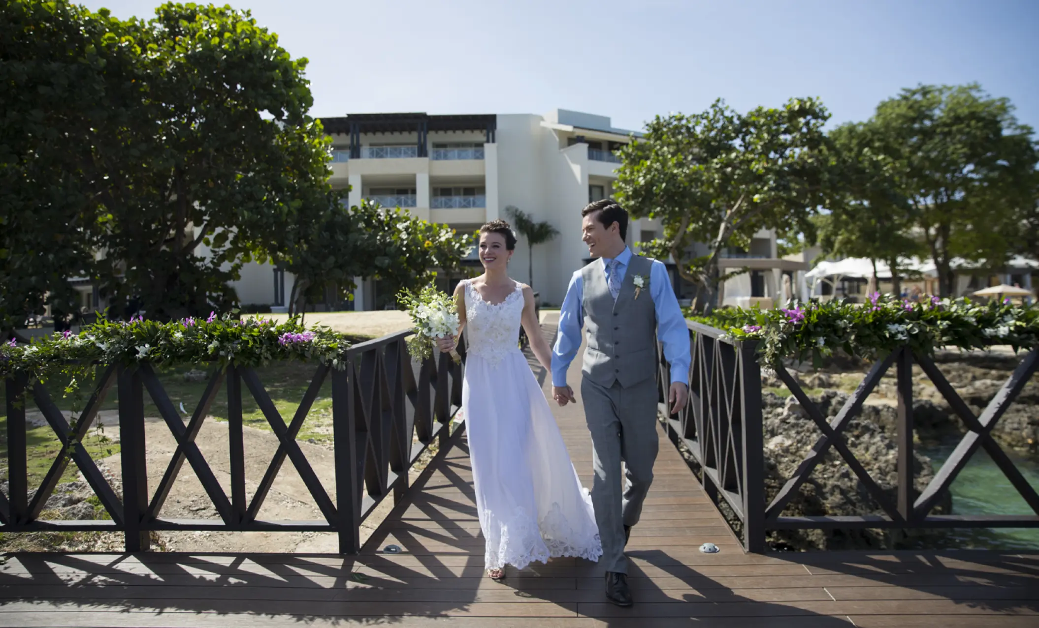 The bride and groom walking hand-in-hand across a wooden bridge at Royalton Hideaway Negril