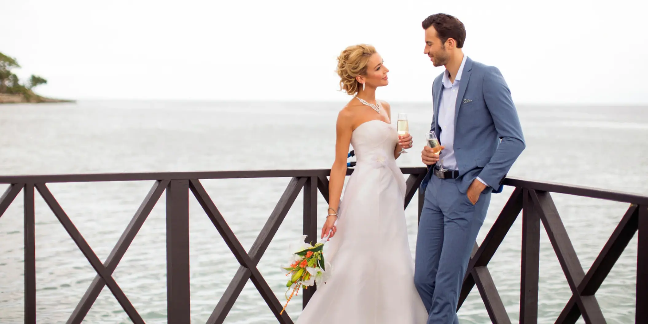 The bride and groom toast with champagne on an ocean pier at Royalton Negril