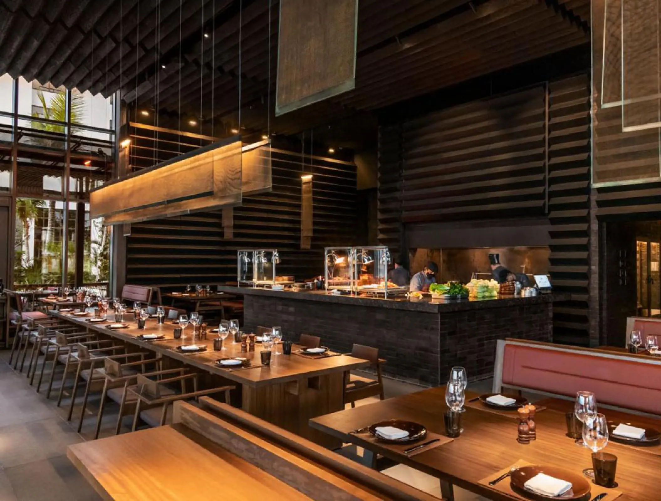 Modern wood-paneled restaurant with long dining tables and open kitchen at Hilton Cancun