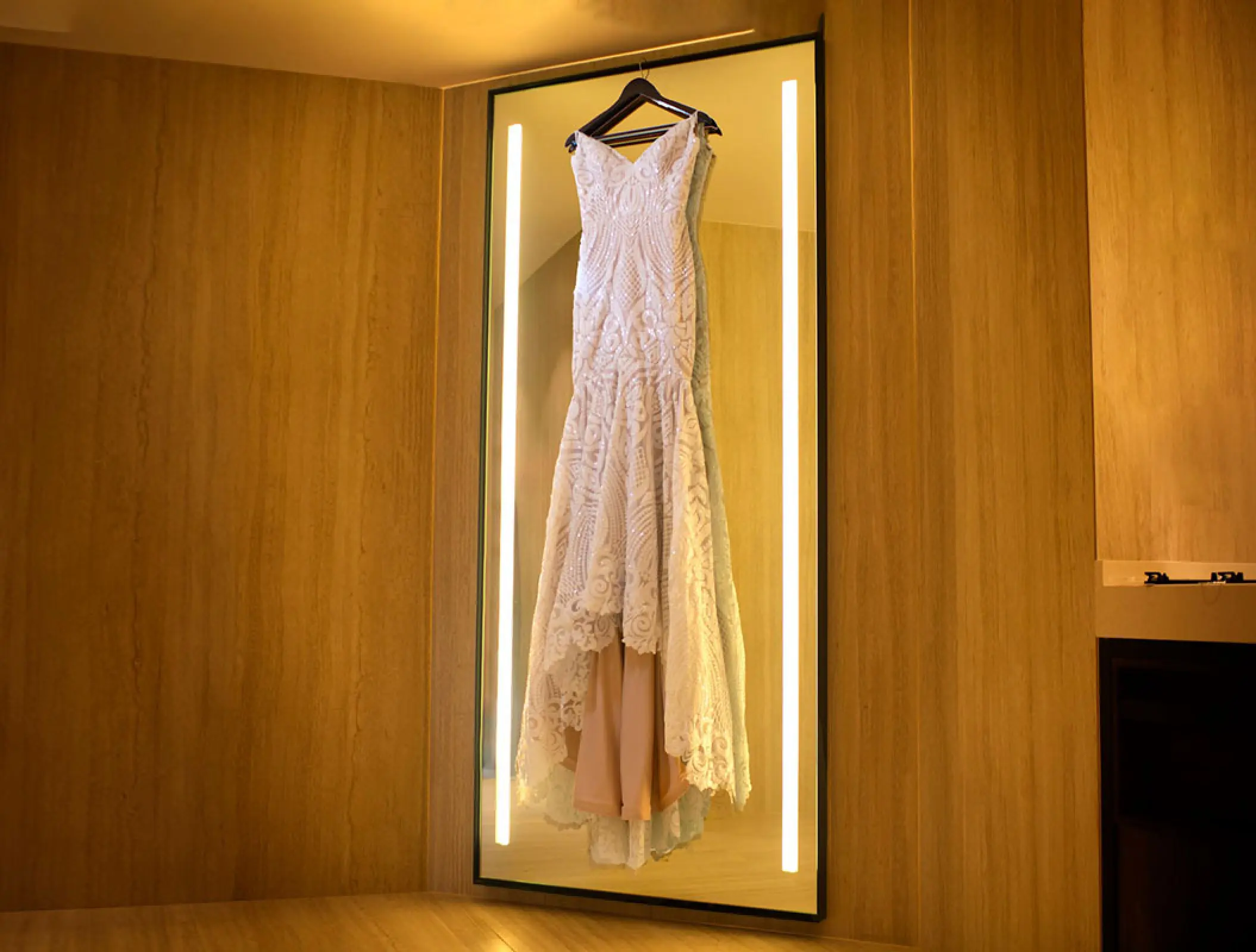 Lace wedding dress hanging in front of a lighted mirror at Hilton Cancun