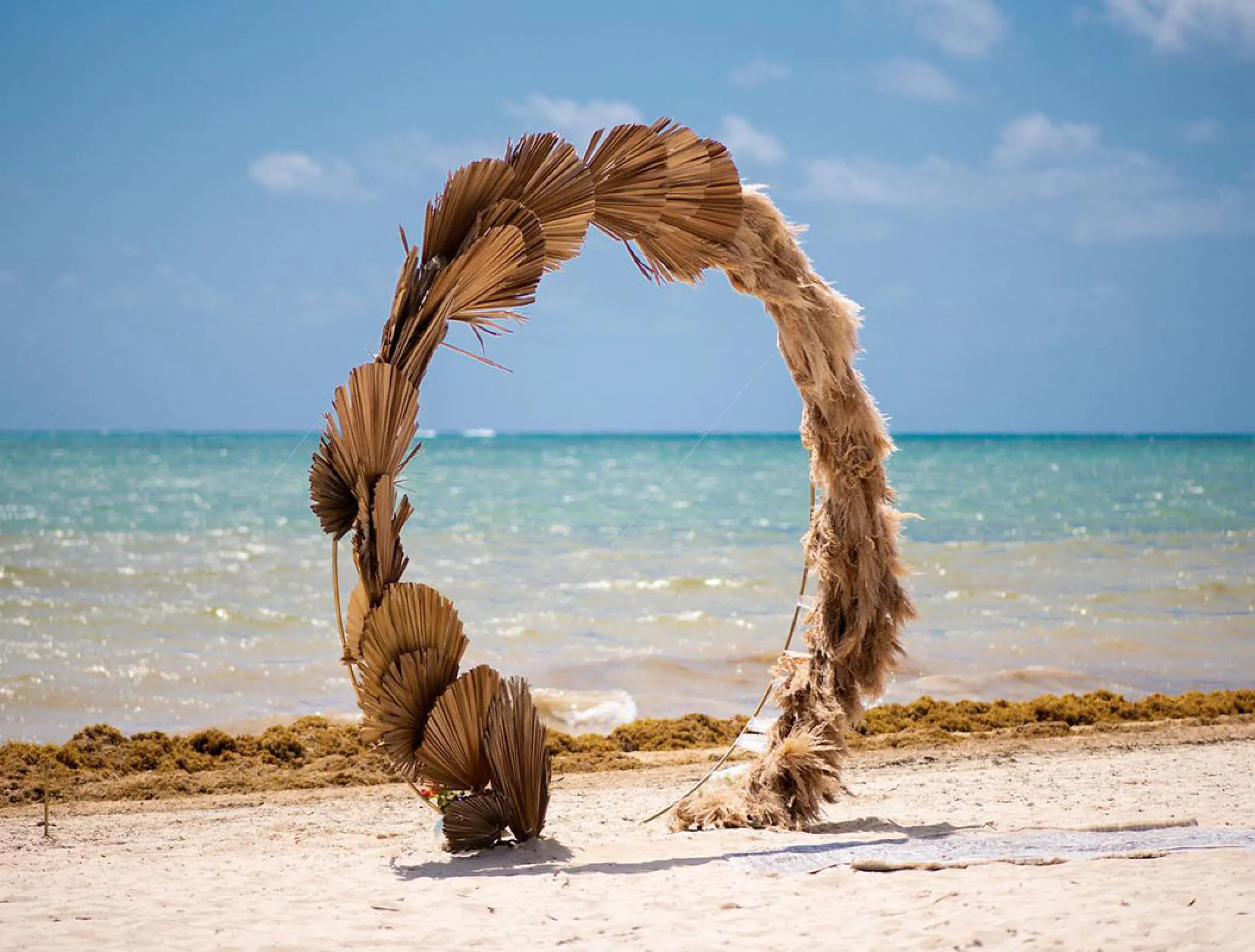 Circular dried palm leaf wedding ceremony arch on the beach at Hilton Cancun