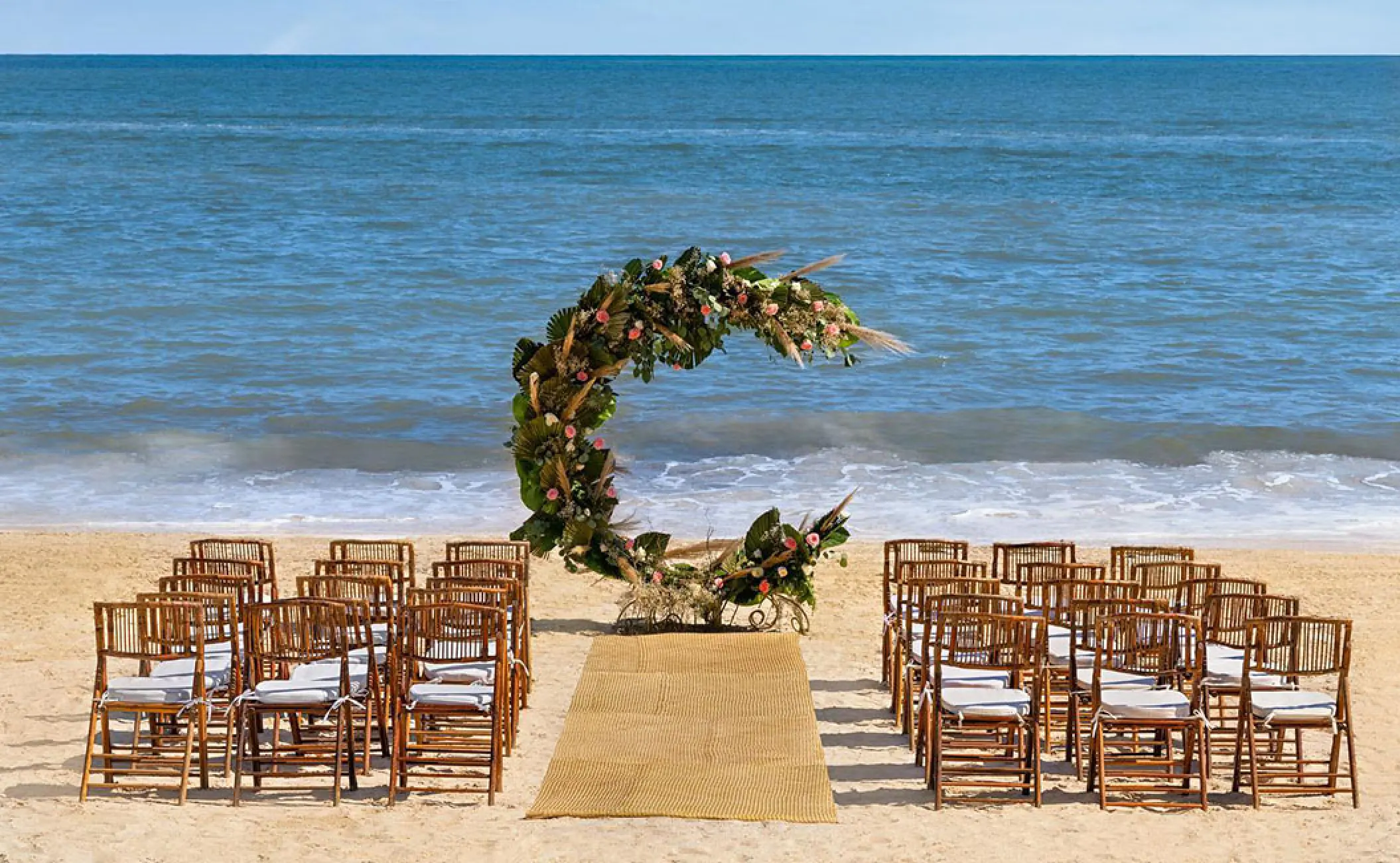 Beachfront wedding ceremony setup with crescent moon floral arch and wooden chairs at Hilton Cancun, Cancun
