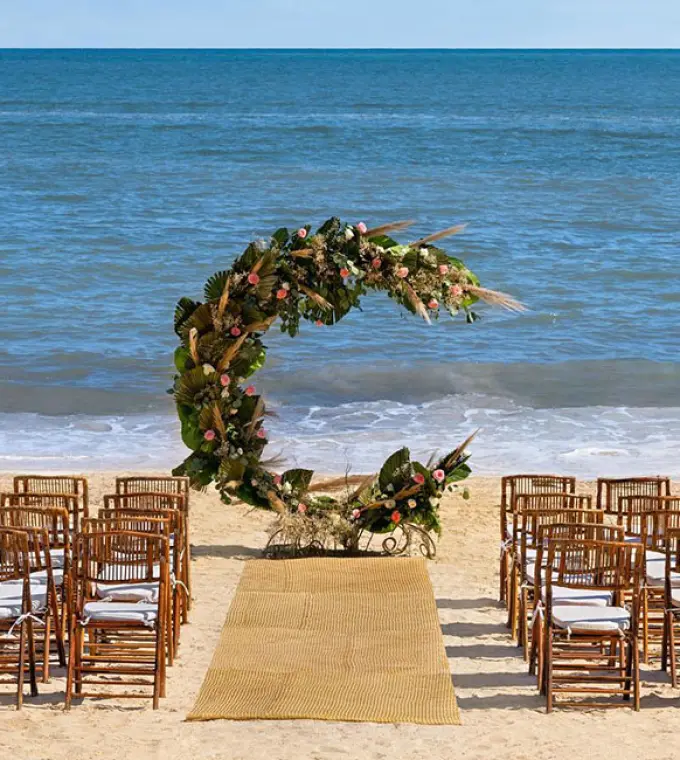 Beachfront wedding ceremony setup with crescent moon floral arch and wooden chairs at Hilton Cancun, Cancun