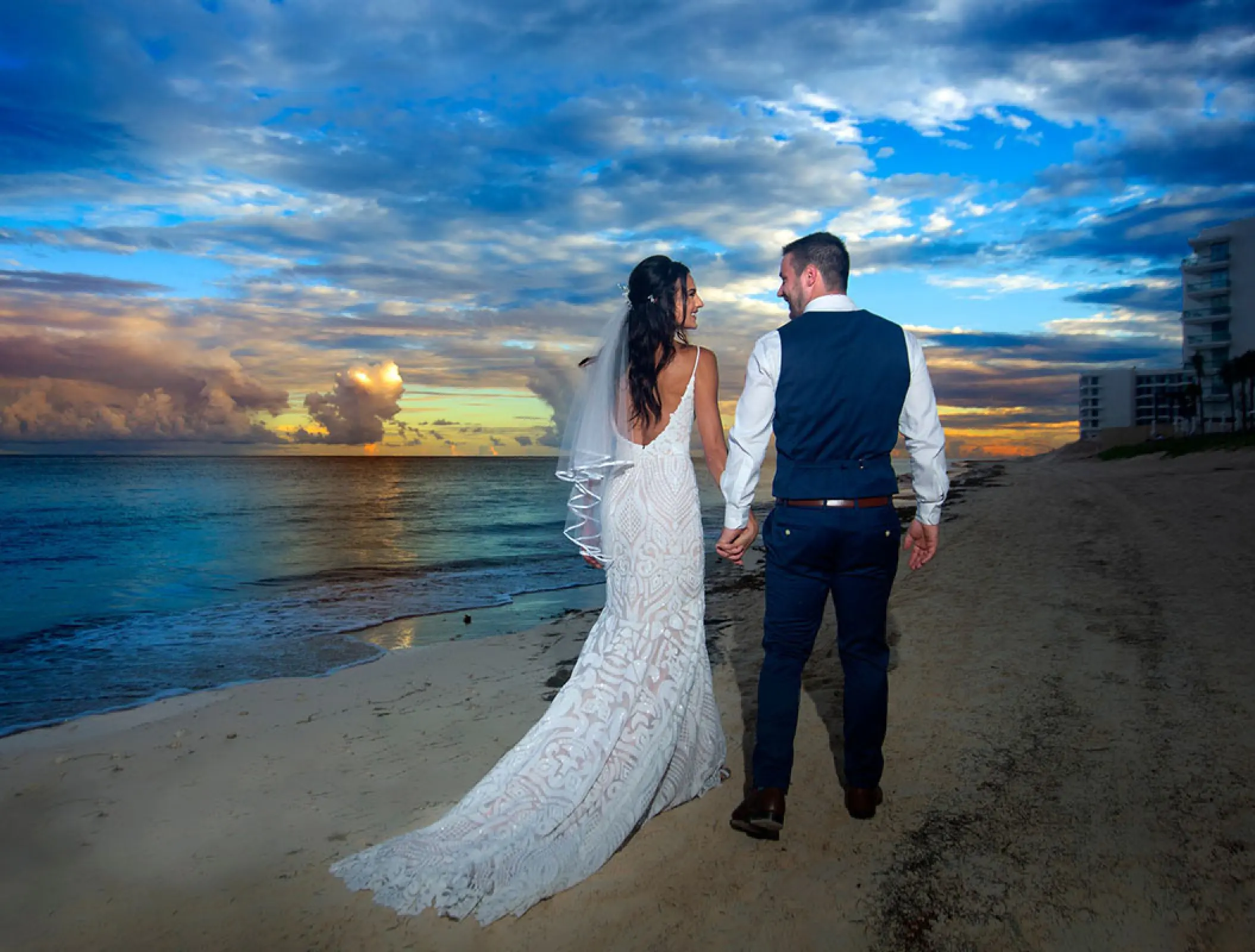 The bride and groom walking hand in hand at sunset at Hilton Cancun, Cancun