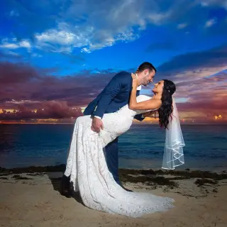 The groom dipping the bride during a sunset kiss on the beach at Hilton Cancun