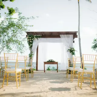 Beach wedding ceremony setup with wooden gazebo and gold chairs at Secrets La Romana