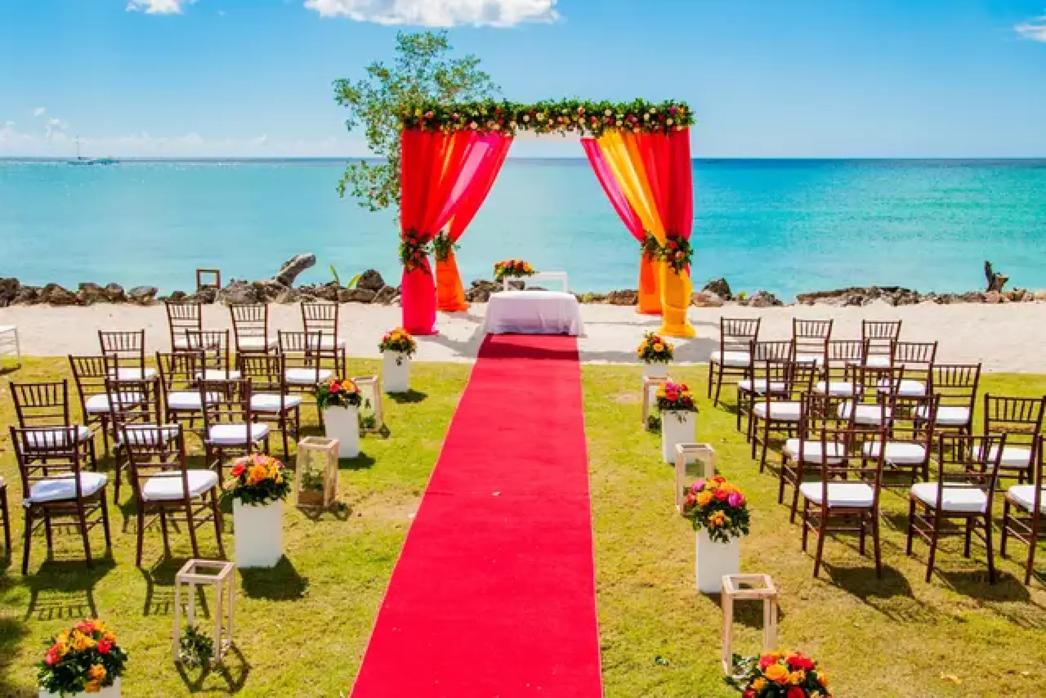 Beachfront wedding ceremony with a red aisle and orange hued arch at Hilton La Romana