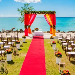Beachfront wedding ceremony with a red aisle and orange hued arch at Hilton La Romana