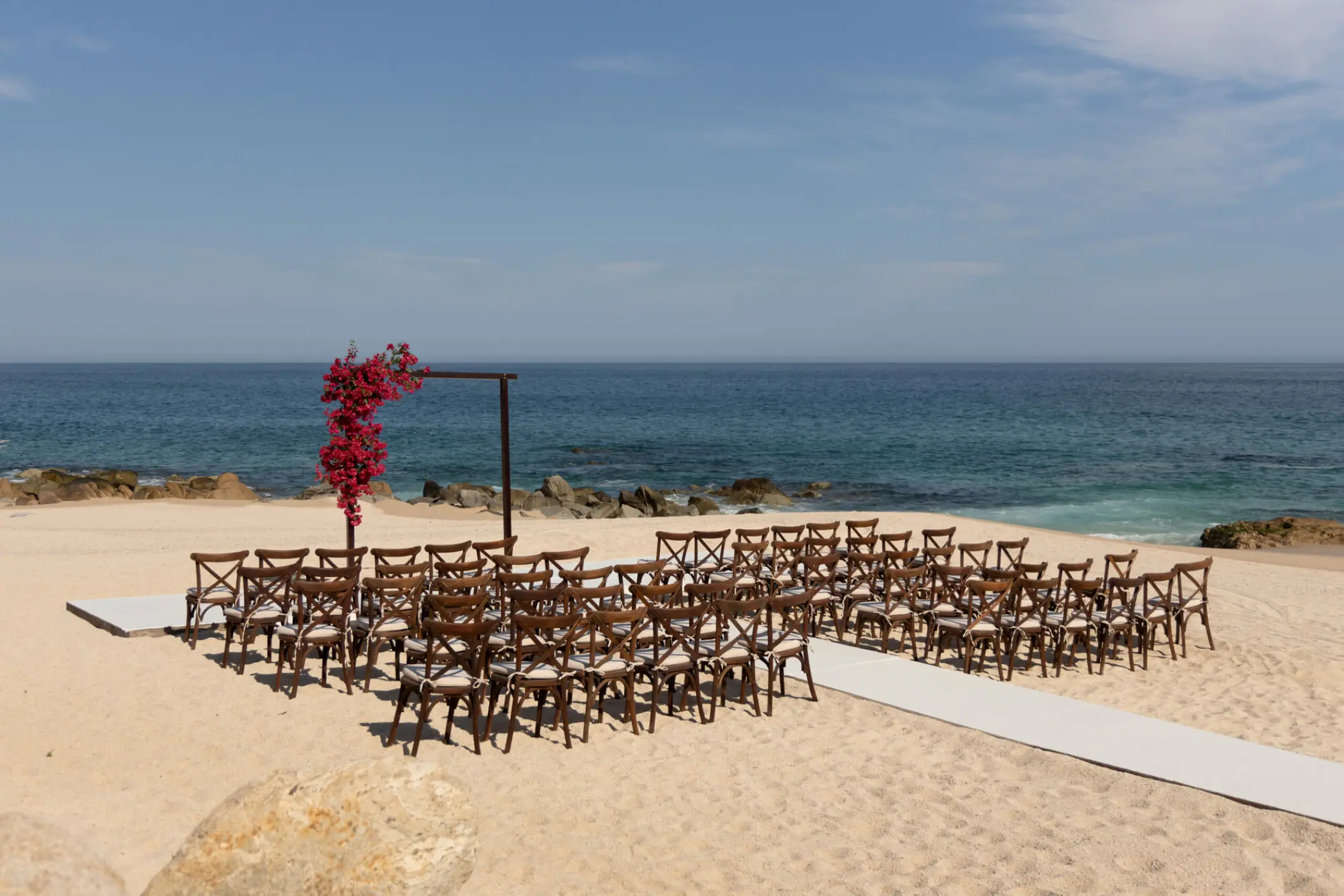 Beachfront wedding ceremony with a floral arch and wooden chairs at Hilton Los Cabos, Cabo San Lucas