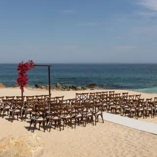 Beachfront wedding ceremony with a floral arch and wooden chairs at Hilton Los Cabos, Cabo San Lucas