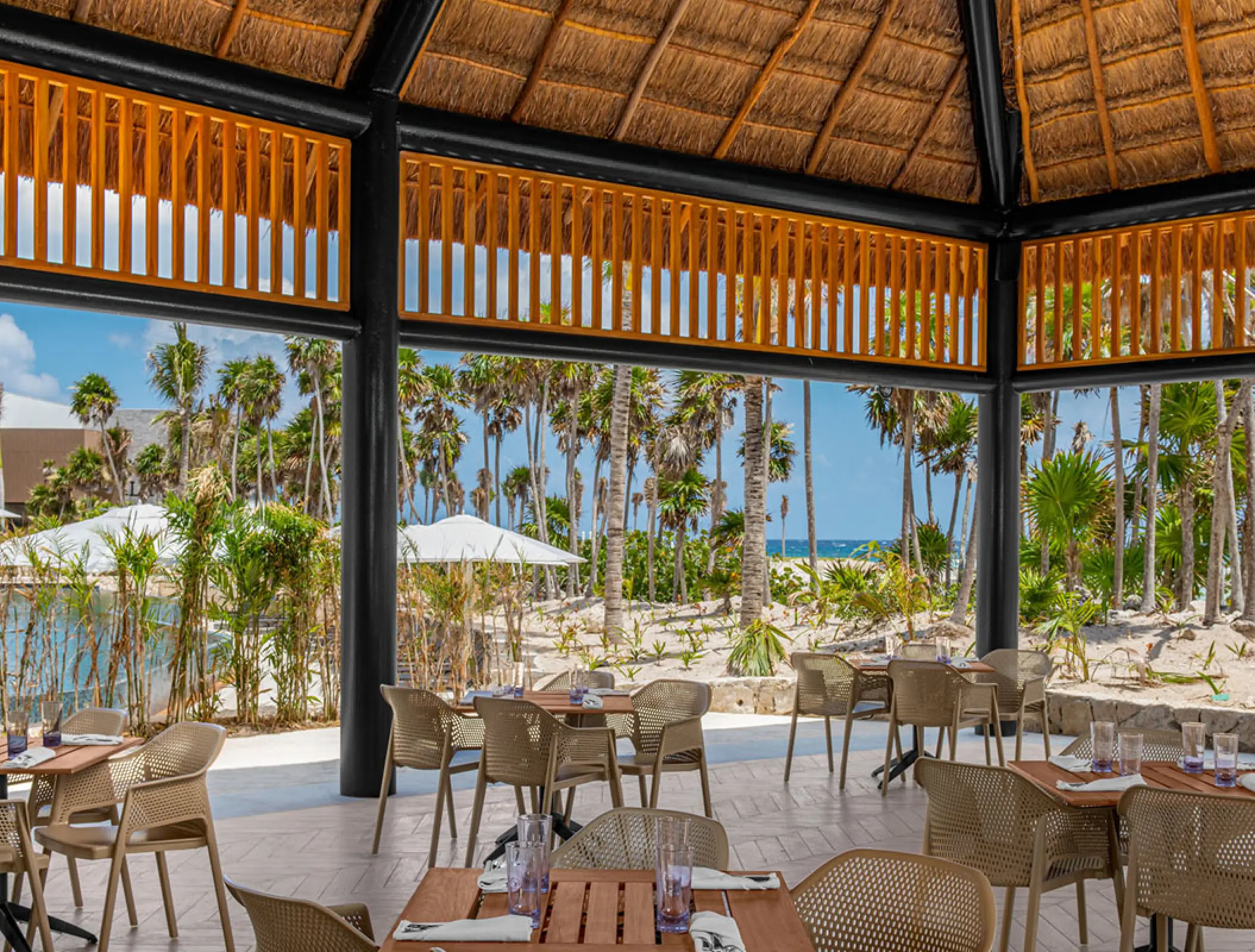 Open-air restaurant dining area at Hilton Tulum overlooking palm trees and the beach