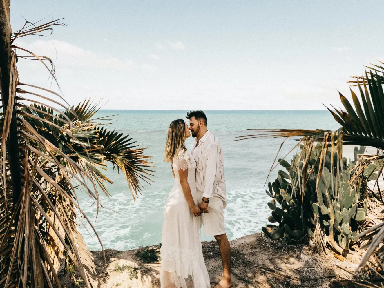 Bride and groom sharing a kiss on a tropical beach cliffside during their destination wedding