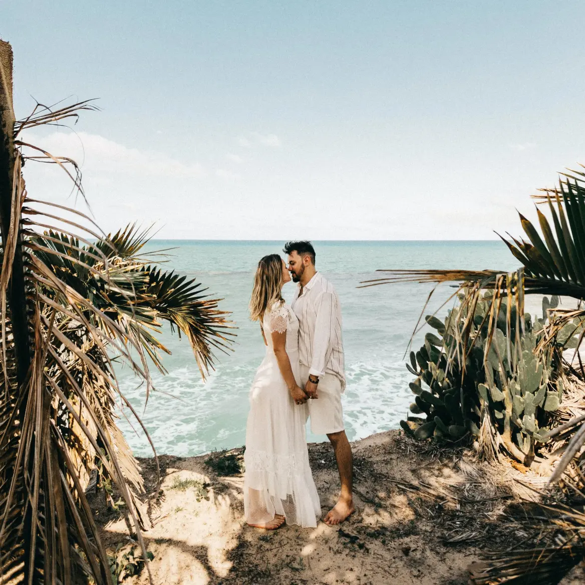 Bride and groom sharing a kiss on a tropical beach cliffside during their destination wedding