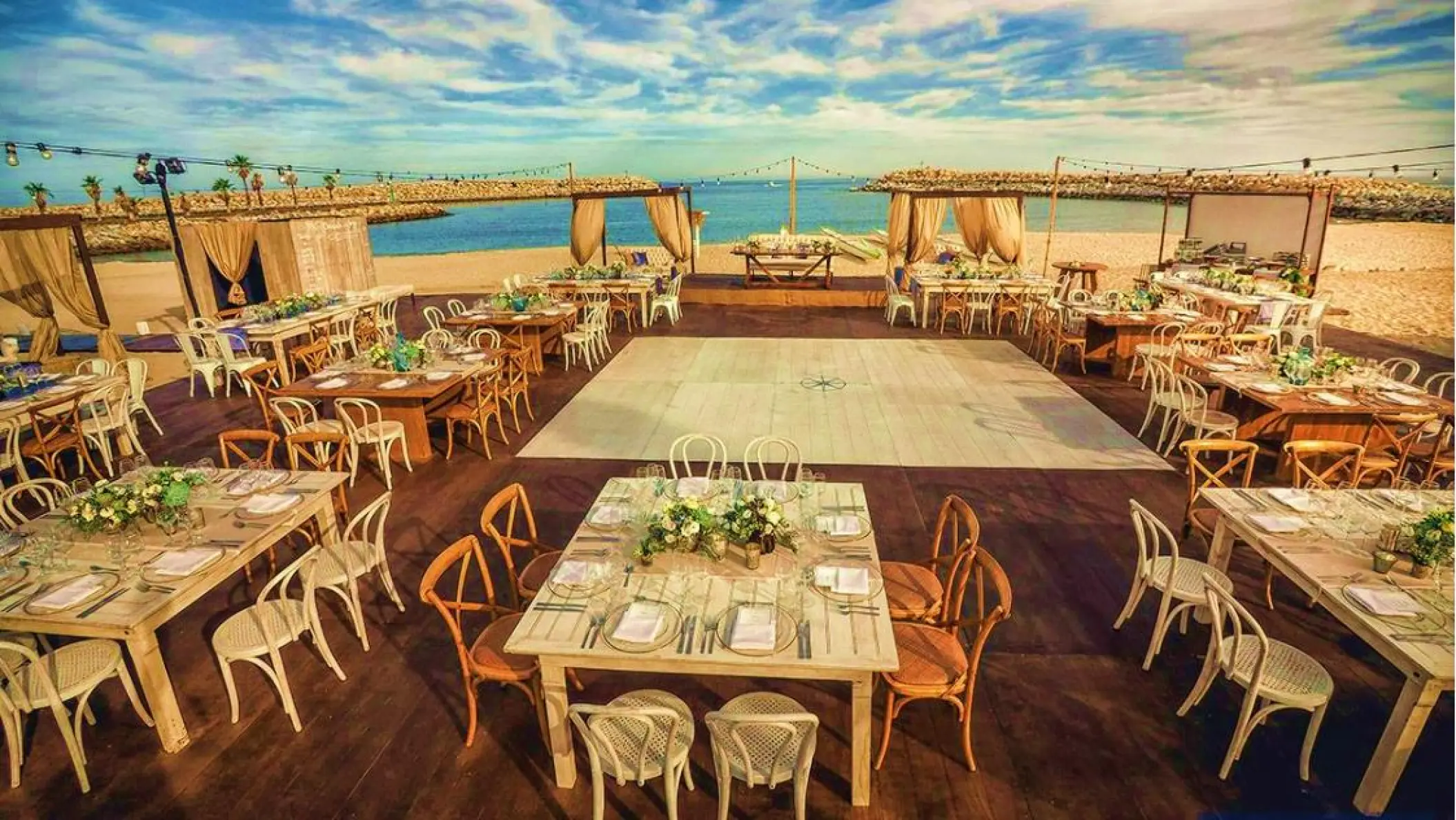 Beachfront wedding reception setup with dance floor and wooden tables at Hotel El Ganzo, Cabo San Lucas