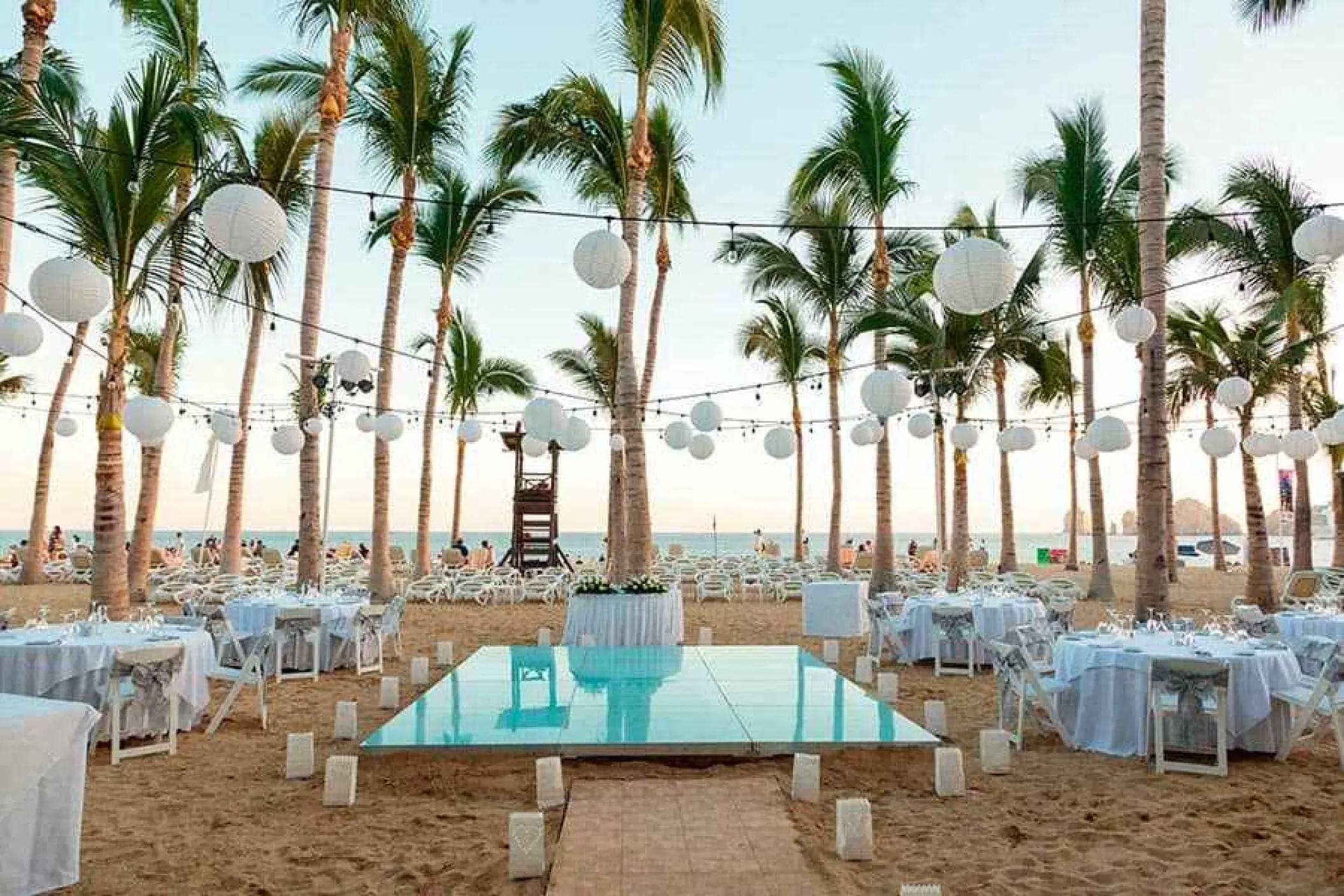 Beach reception setup with a dance floor and paper lanterns at Riu Palace Cabo San Lucas