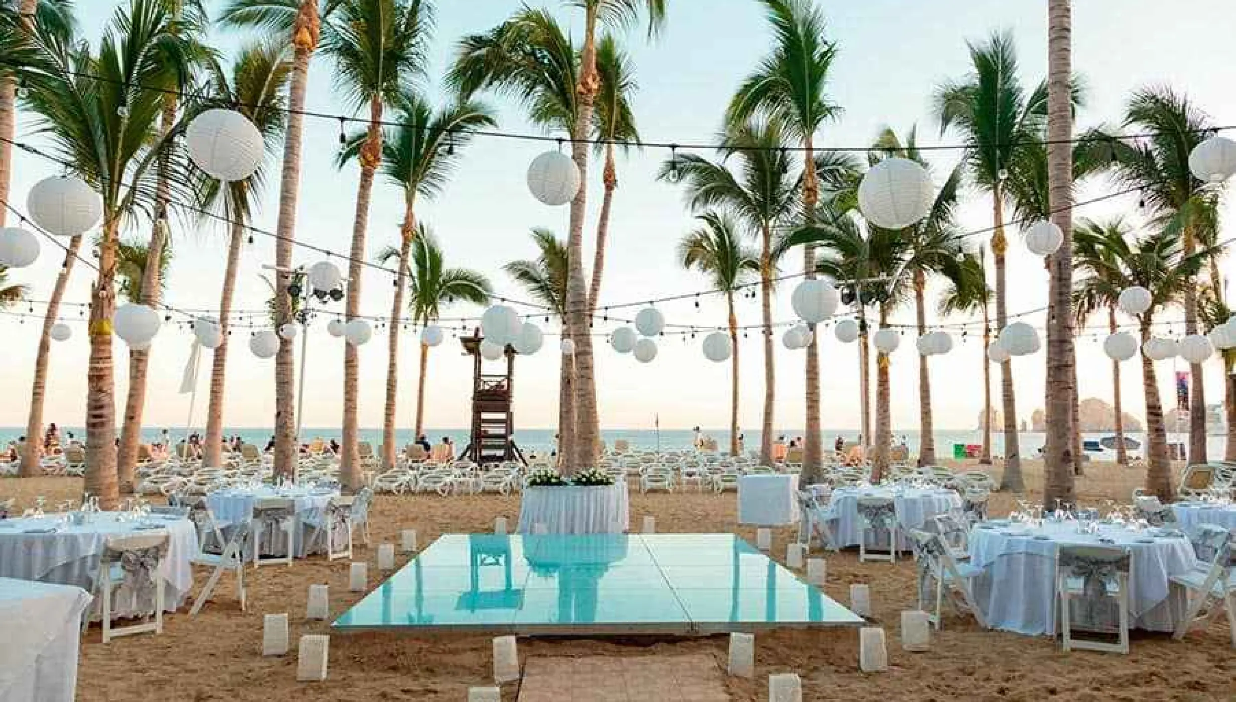 Beach reception setup with a dance floor and paper lanterns at Riu Palace Cabo San Lucas