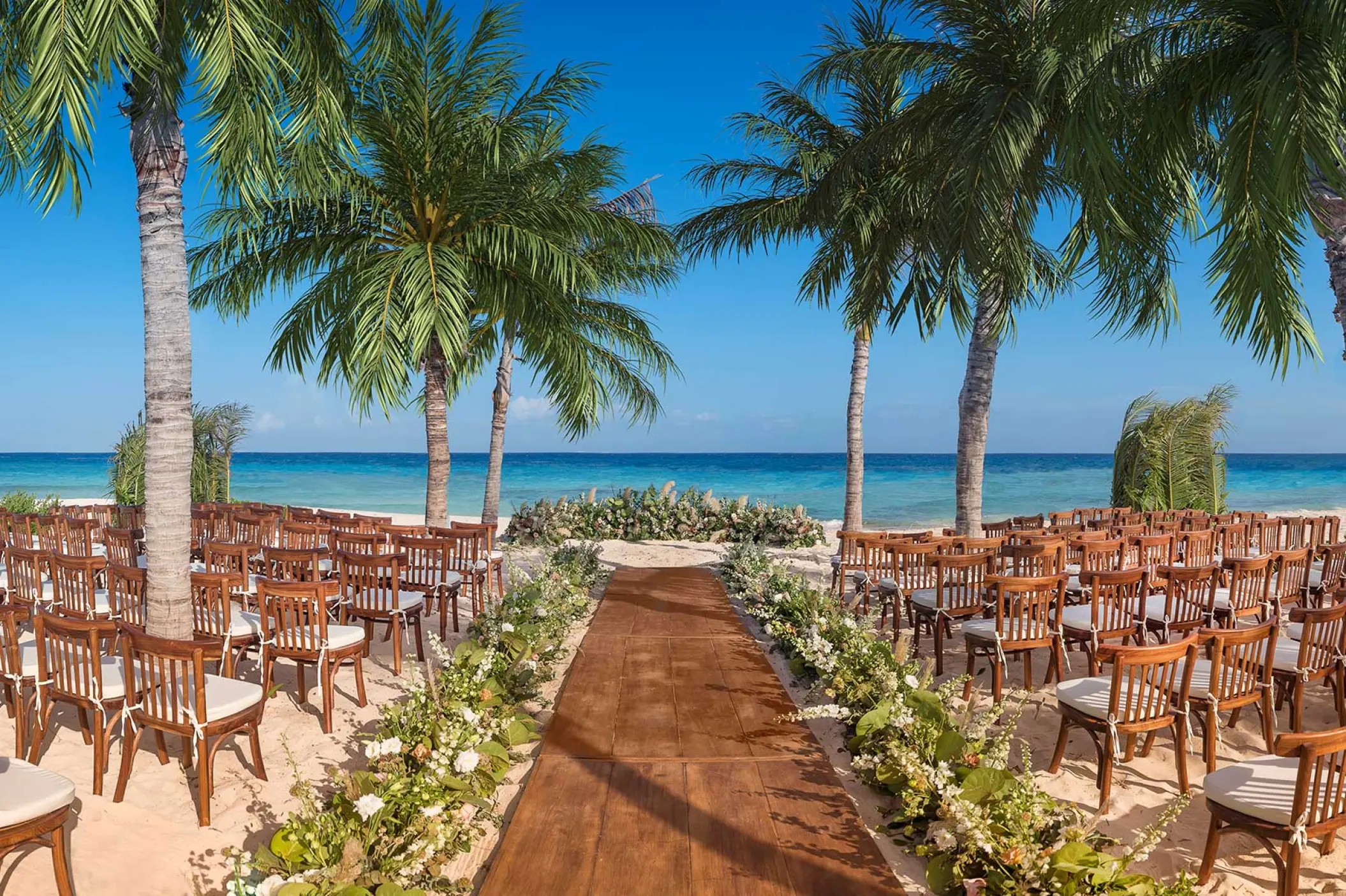 Beachfront wedding ceremony setup with wooden aisle and chairs at Hotel Xcaret Arte, Riviera Maya