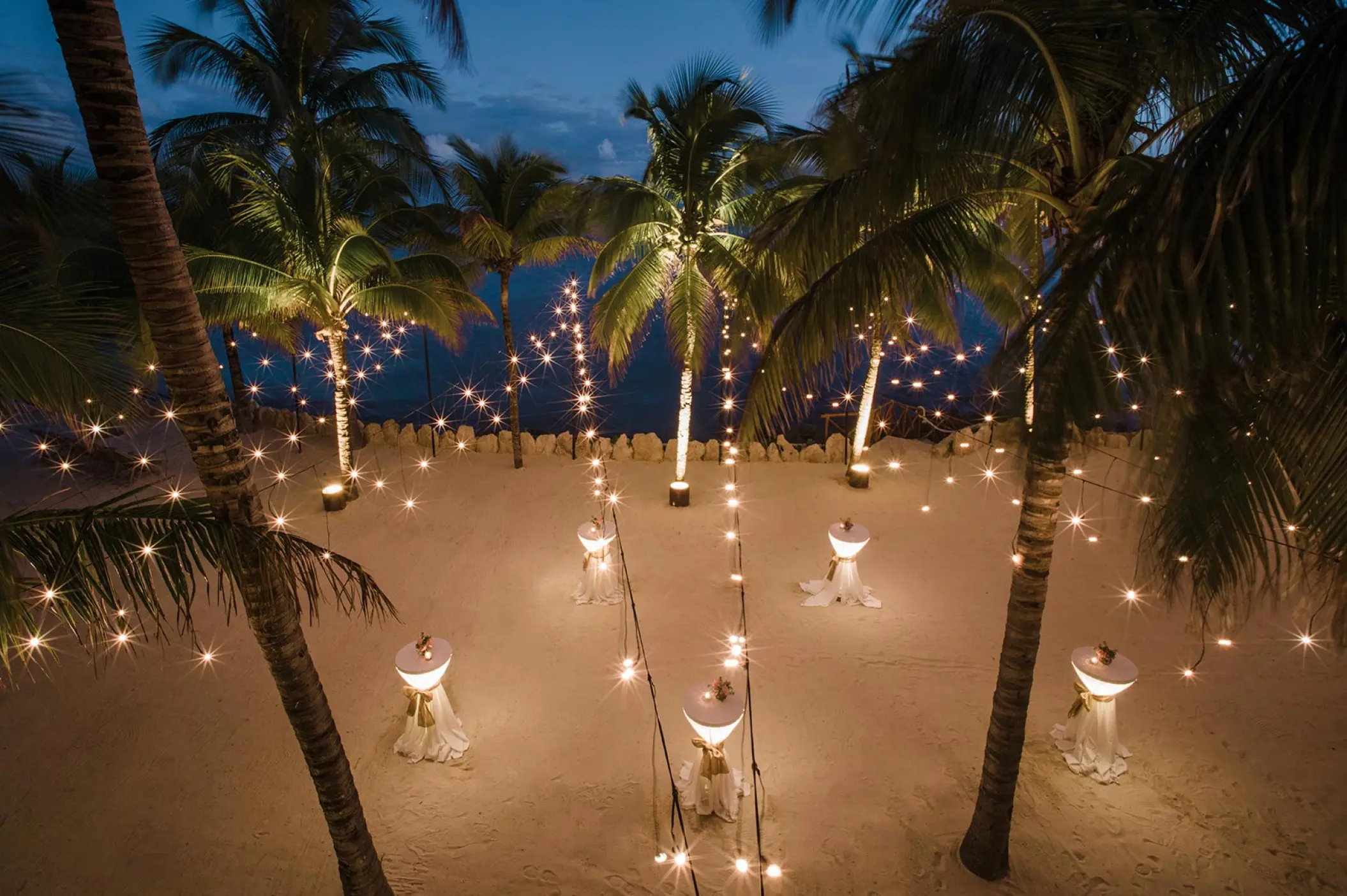 Evening wedding cocktail reception with string lights and palm trees at Hotel Xcaret Arte, Riviera Maya