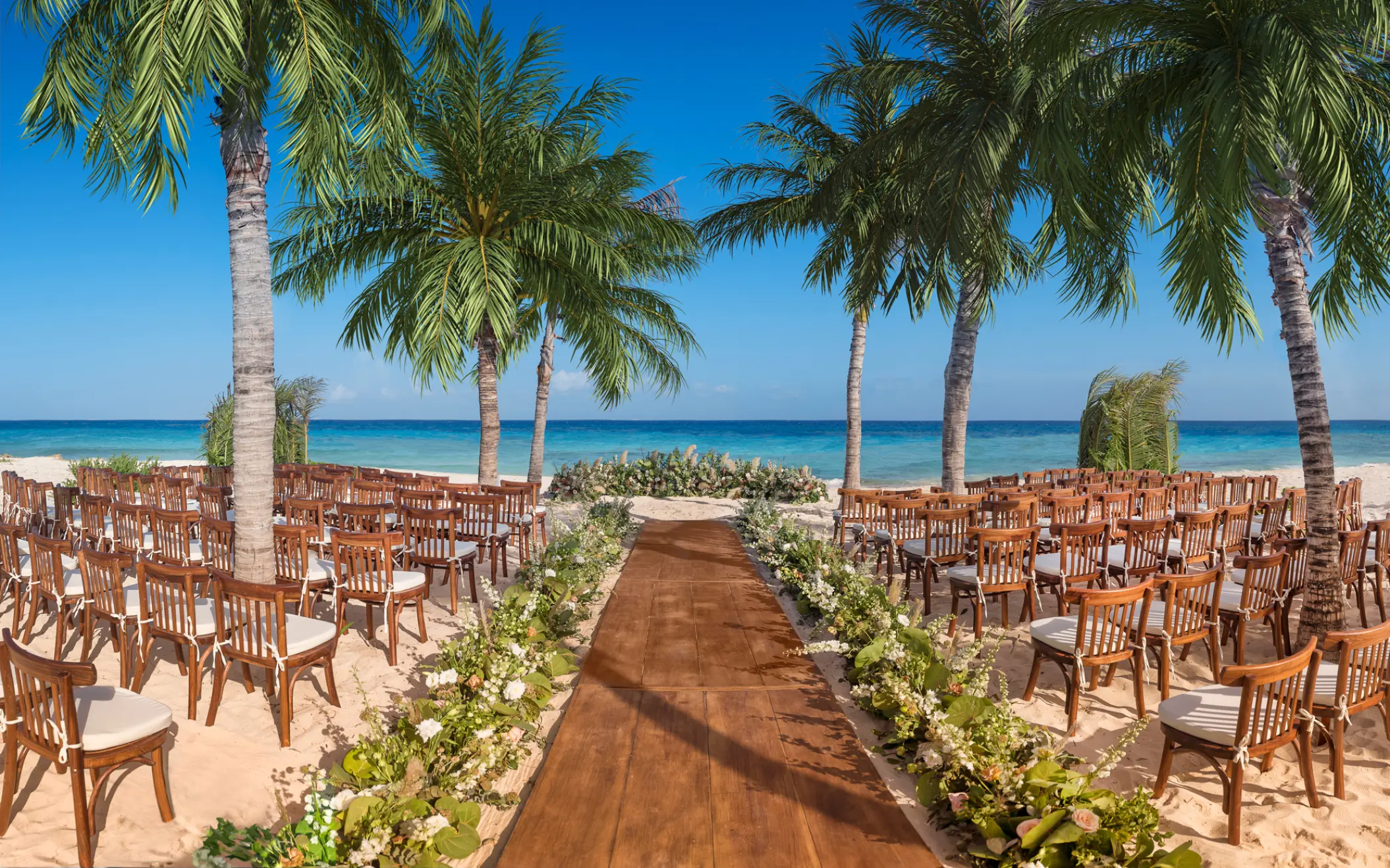 Beachfront wedding ceremony setup with wooden chairs and aisle at Hotel Xcaret Mexico, Riviera Maya