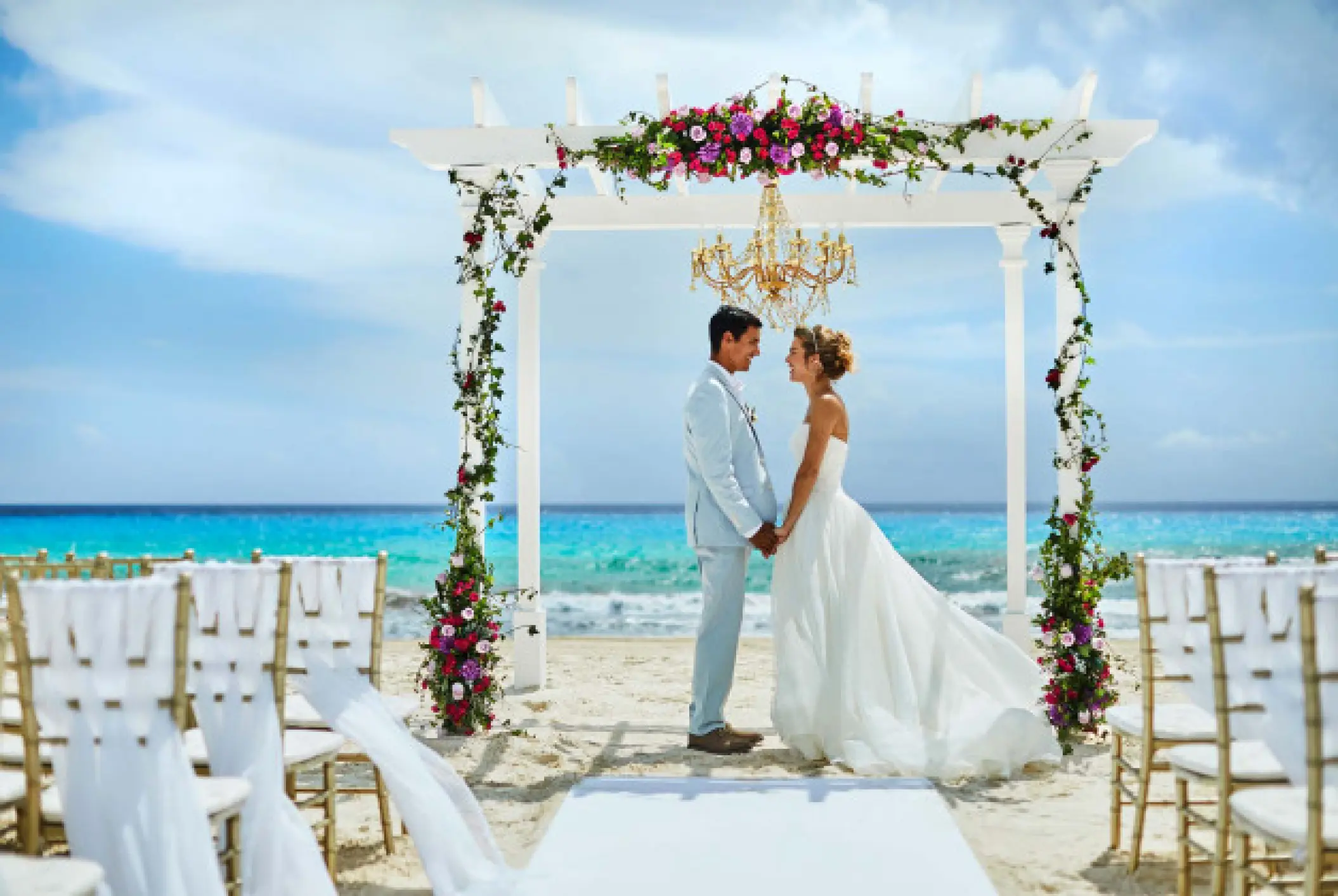 The bride and groom standing under a floral white gazebo for a beach ceremony at Hyatt Zilara Cancun