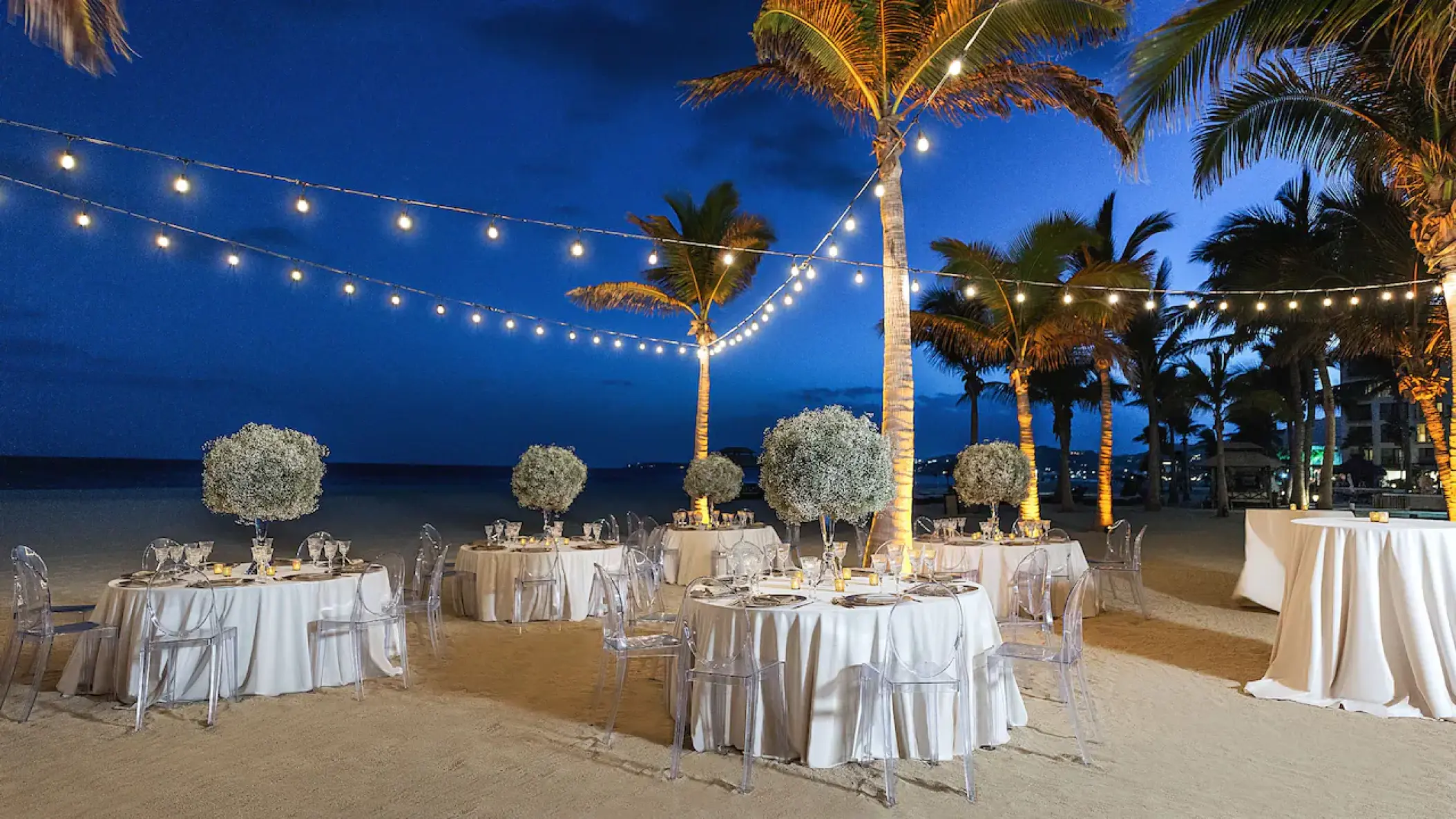 Beachfront wedding reception with string lights and white floral centerpieces at Hyatt Ziva Los Cabos, Cabo San Lucas