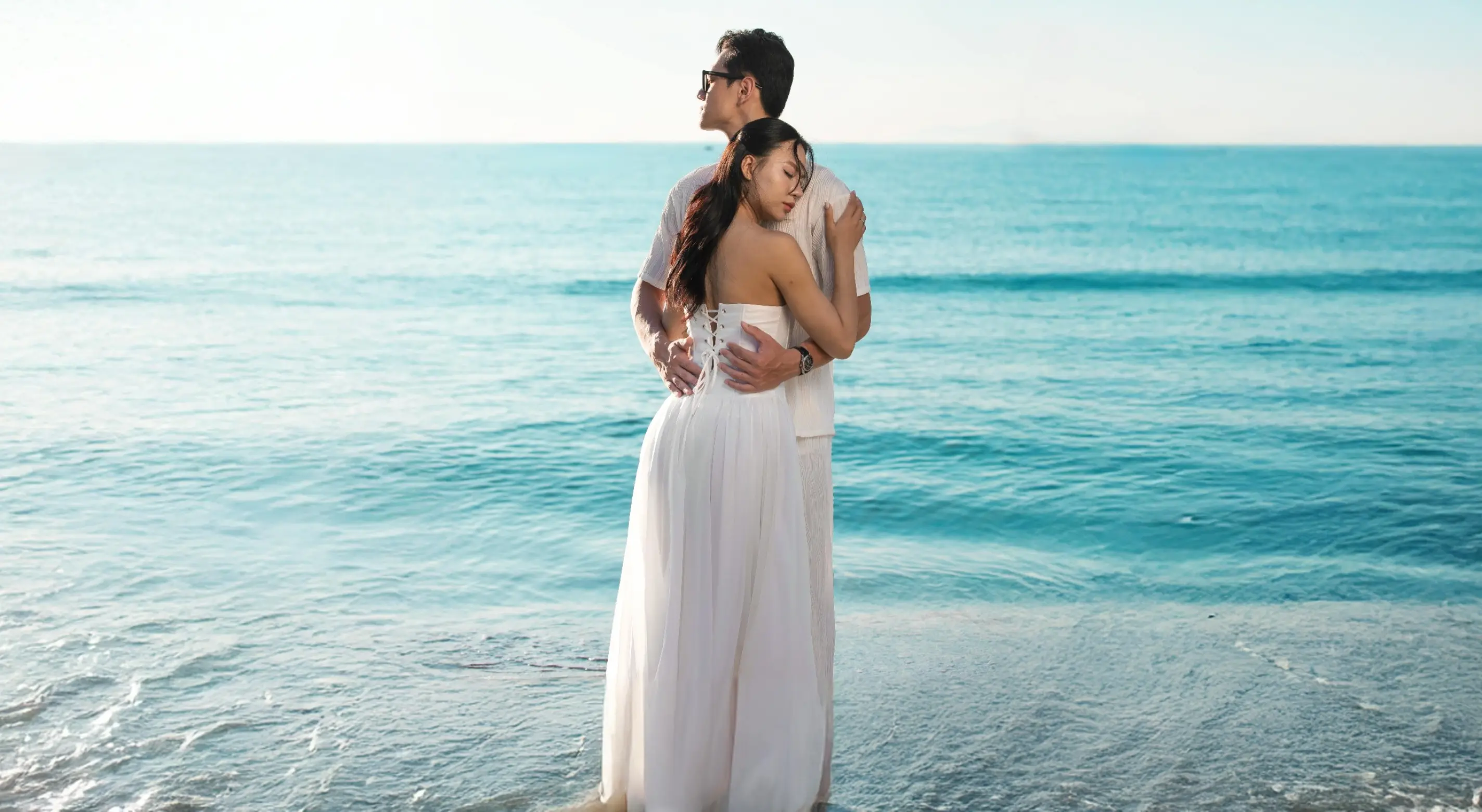 Bride and groom embracing on a beach with turquoise ocean water in the background