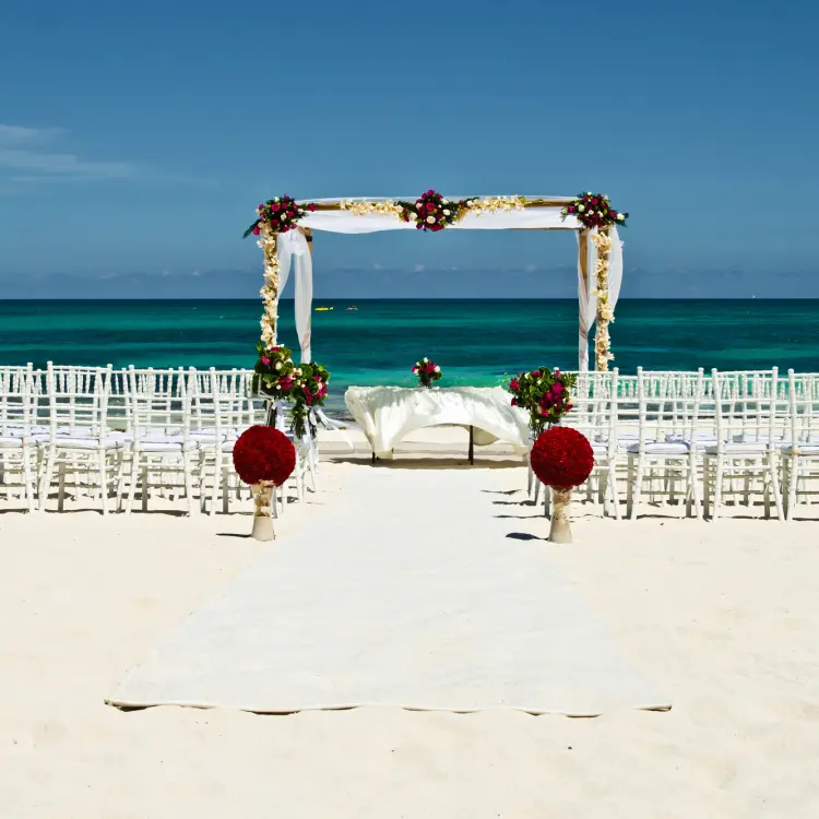 Beachfront wedding ceremony with white chairs and floral arch at JOIA Paraiso by Iberostar, Riviera Maya
