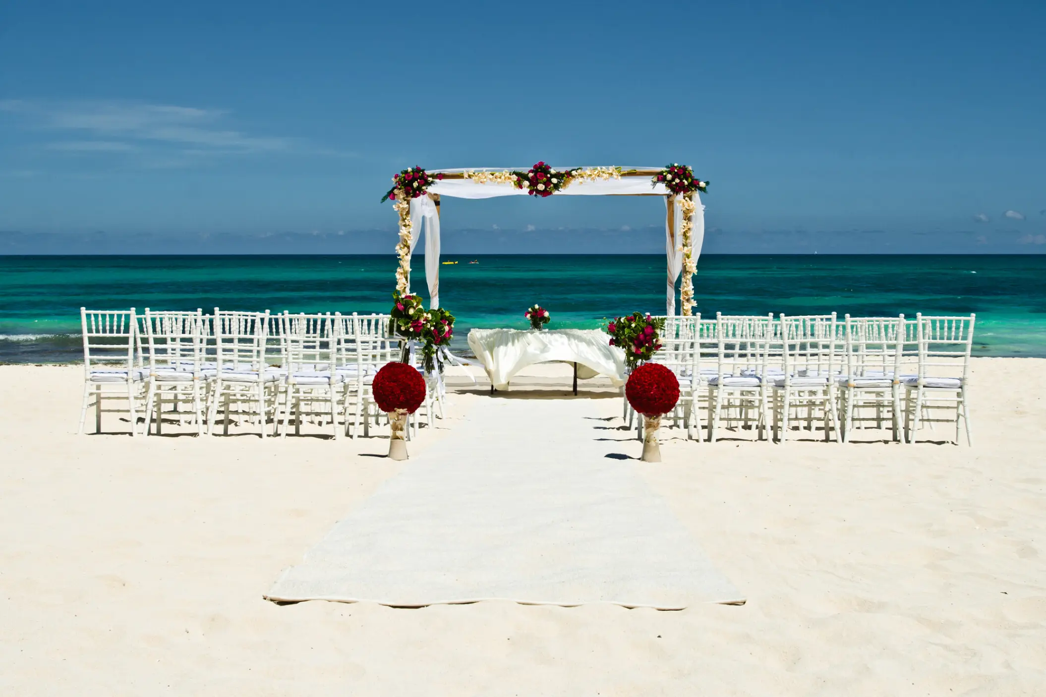 Beachfront wedding ceremony with white chairs and floral arch at JOIA Paraiso by Iberostar, Riviera Maya