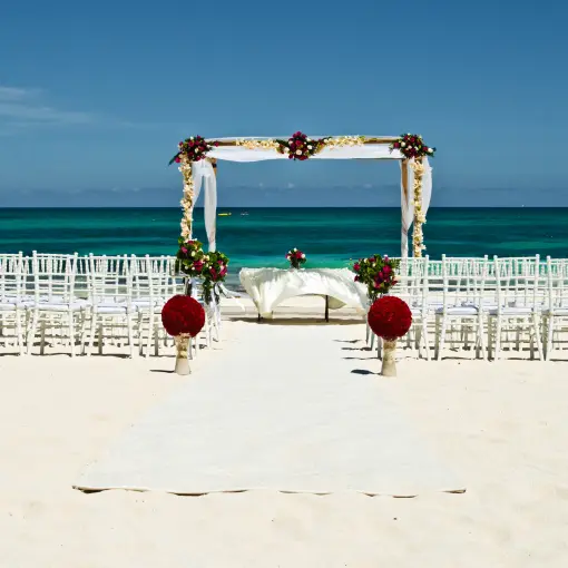 Beachfront wedding ceremony with white chairs and floral arch at JOIA Paraiso by Iberostar, Riviera Maya
