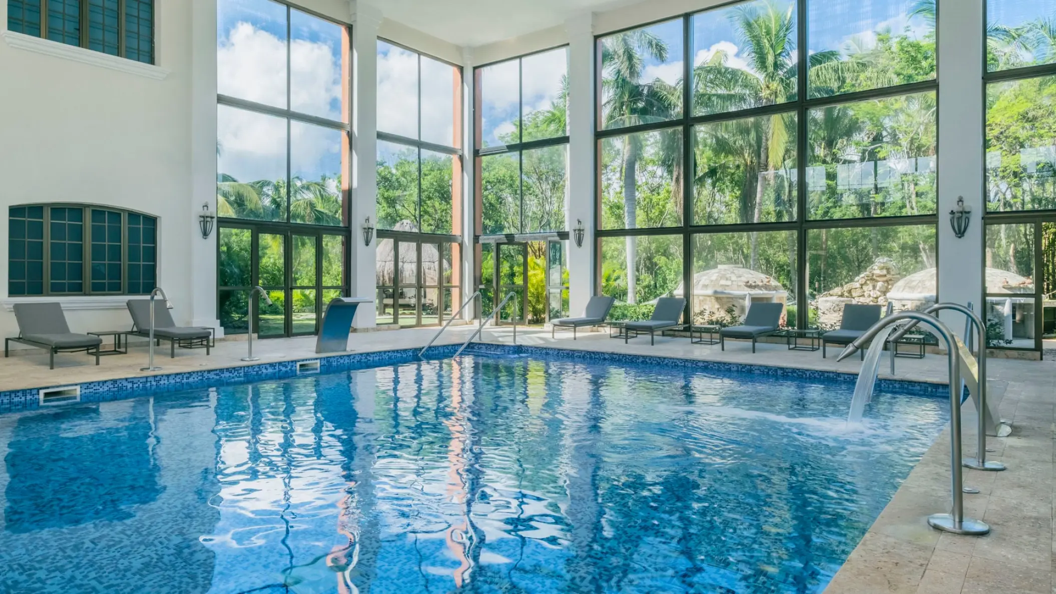 Indoor pool with floor-to-ceiling windows and lounge chairs at Iberostar Waves Paraiso Beach, Riviera Maya