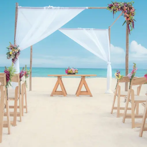 Beachfront wedding ceremony with white draped arch and wooden chairs at Iberostar Paraiso Del Mar, Riviera Maya