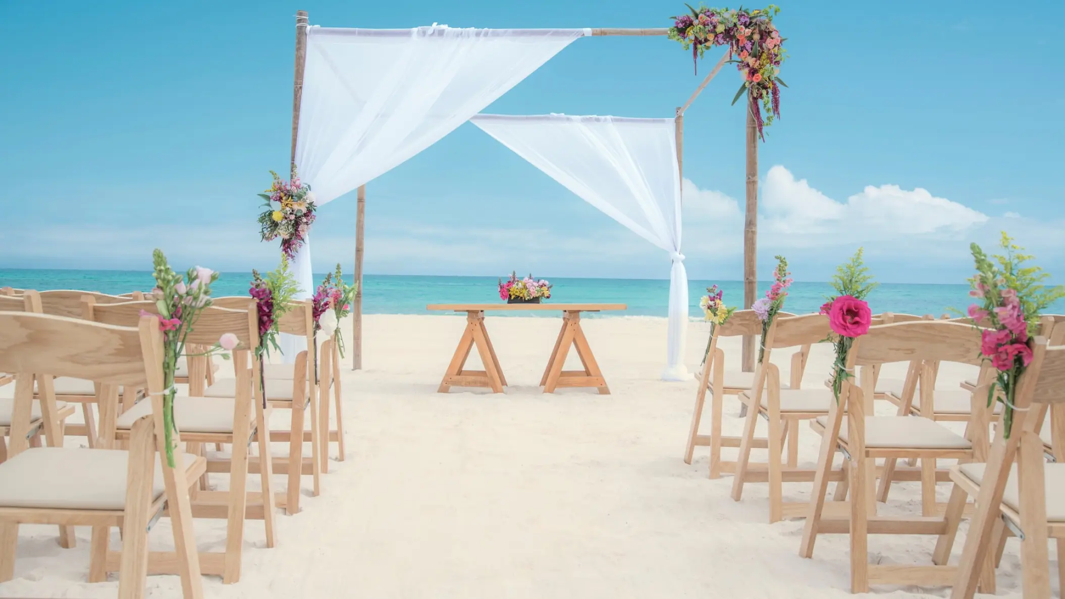 Beachfront wedding ceremony with white draped arch and wooden chairs at Iberostar Paraiso Del Mar, Riviera Maya